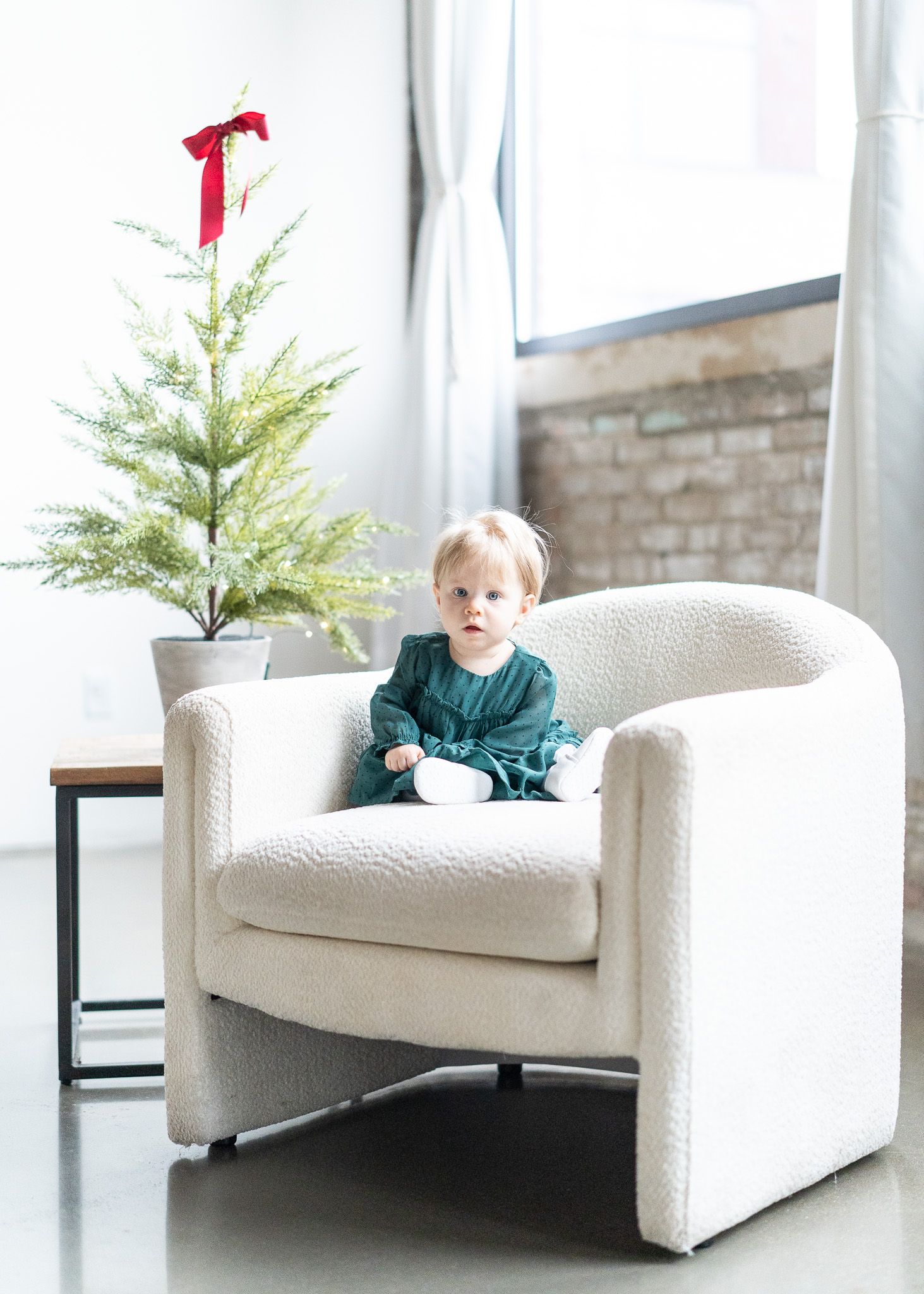 Four identical white armchairs arranged in a row with small evergreen trees and red bows as holiday decor.