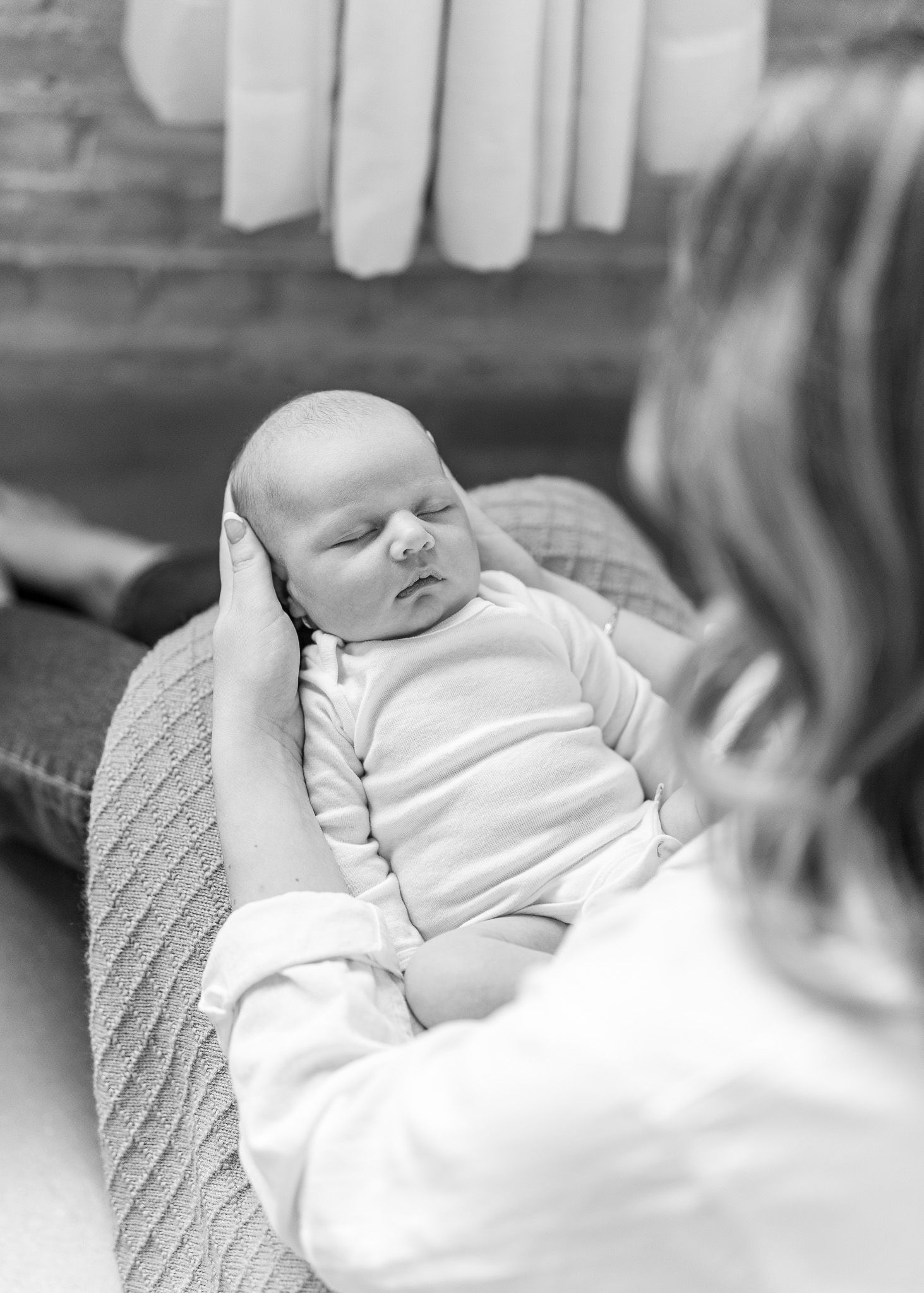 A sleeping baby wearing white clothing rests peacefully on a patterned couch cushion.