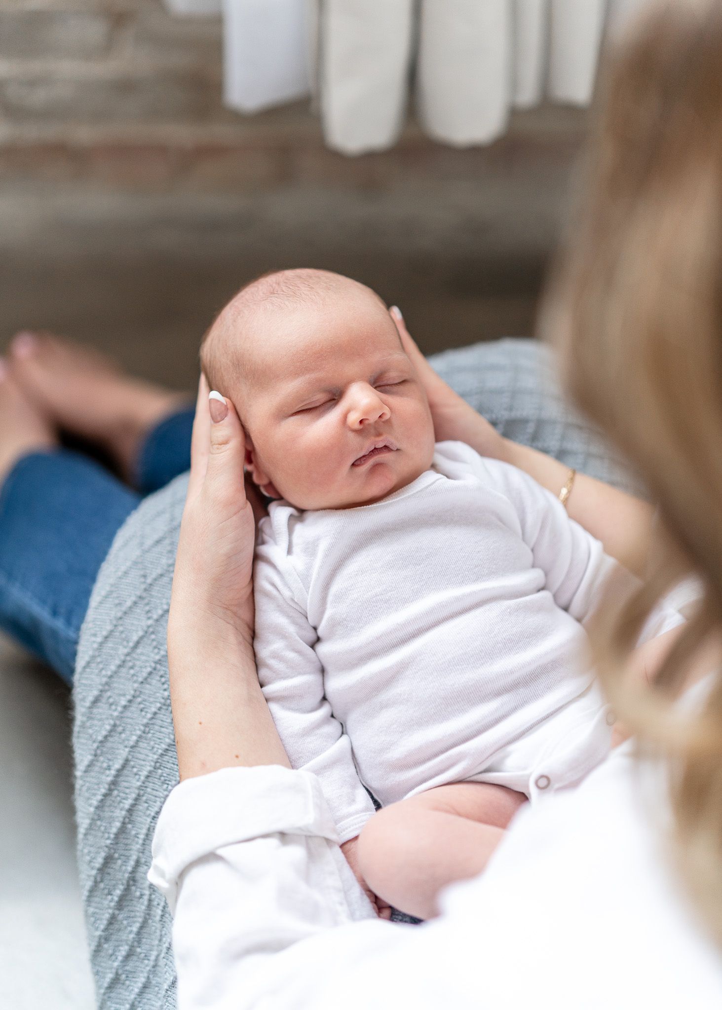 A sleeping newborn baby wearing a white onesie rests peacefully on a blue blanket.