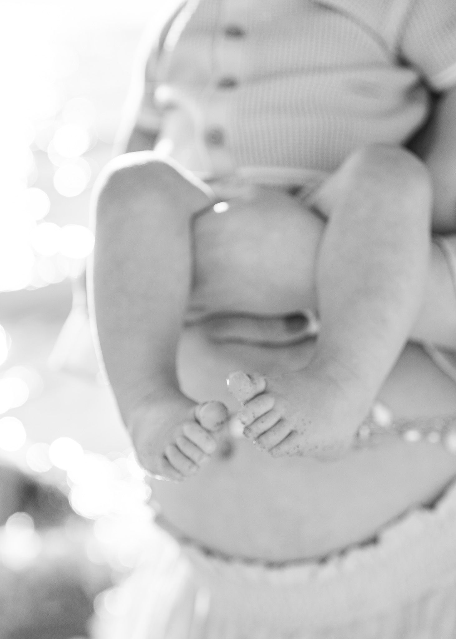 Close-up black and white photo of tiny newborn baby feet resting on soft fabric with delicate details.