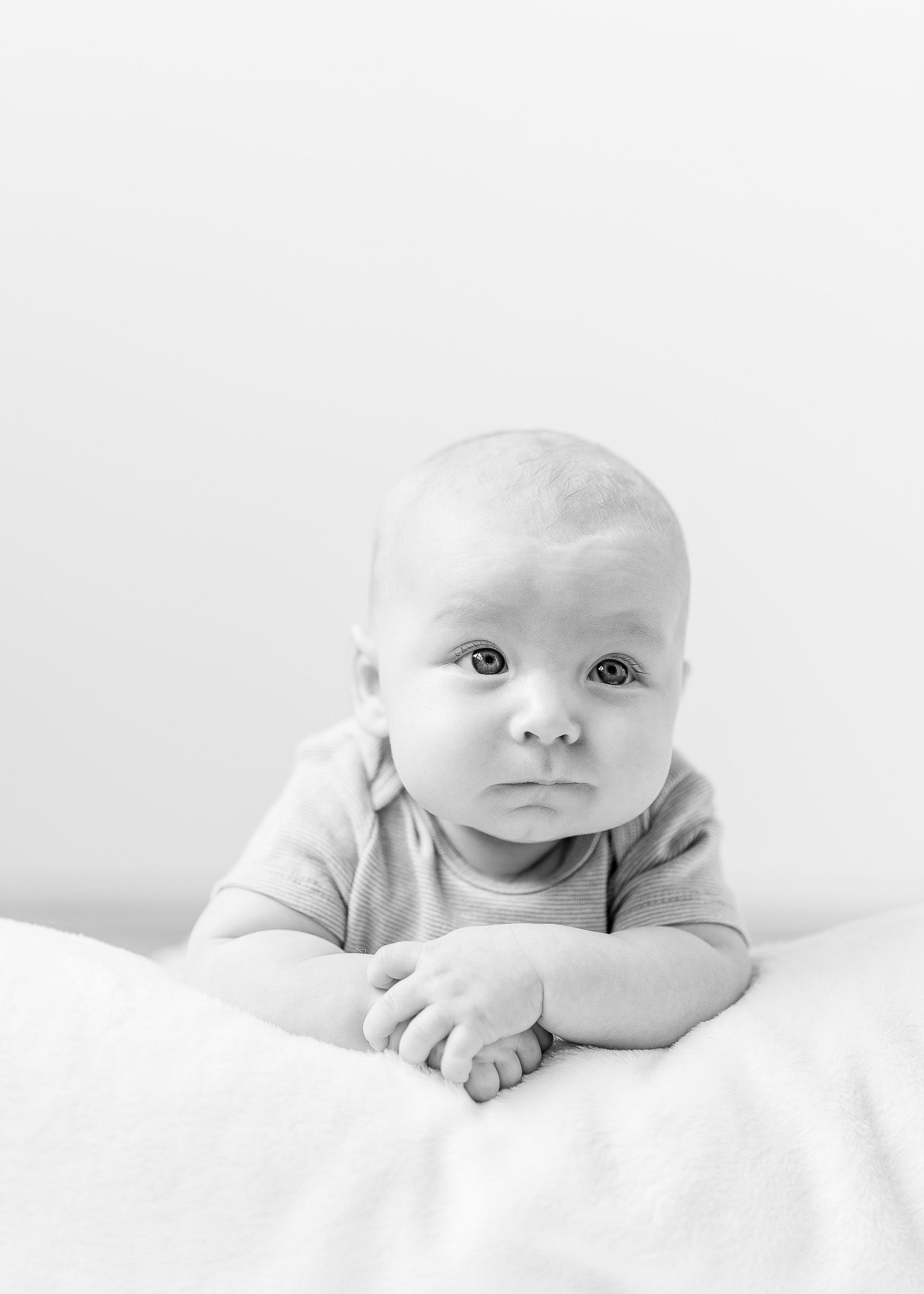 Four black and white photos show a baby lying on white bedding in different poses and expressions.