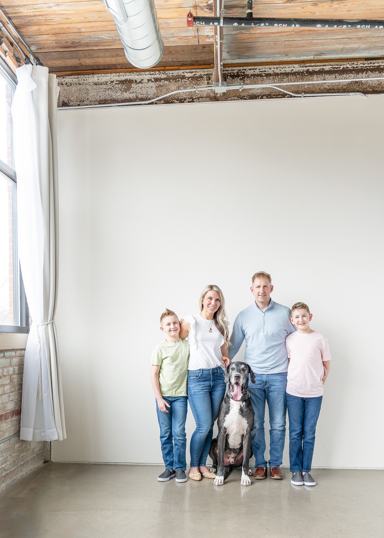 A family stands together in a bright studio space with their large Great Dane dog against a white wall.