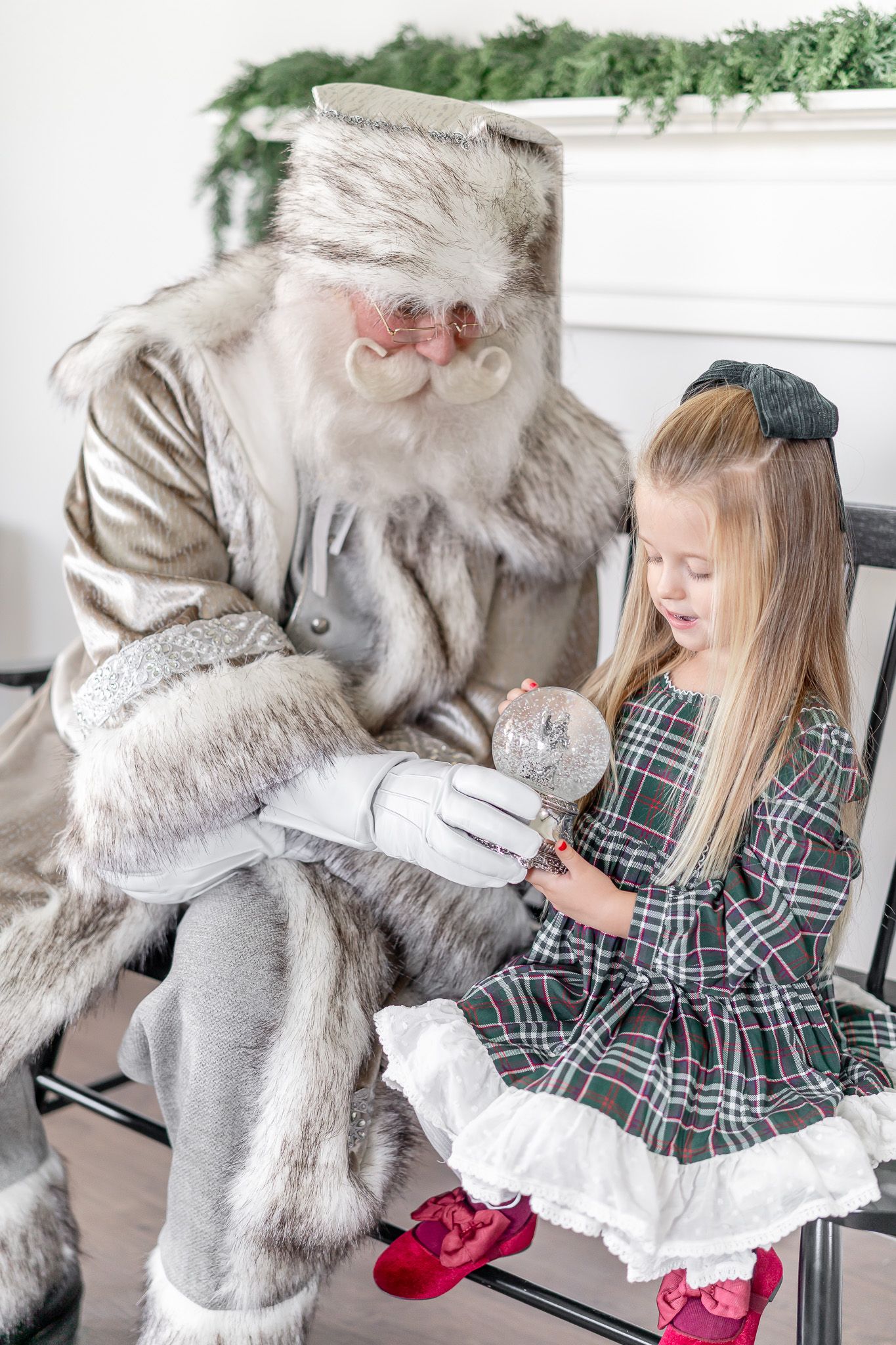 Santa in vintage gray attire shares a special moment with a child in a plaid dress.