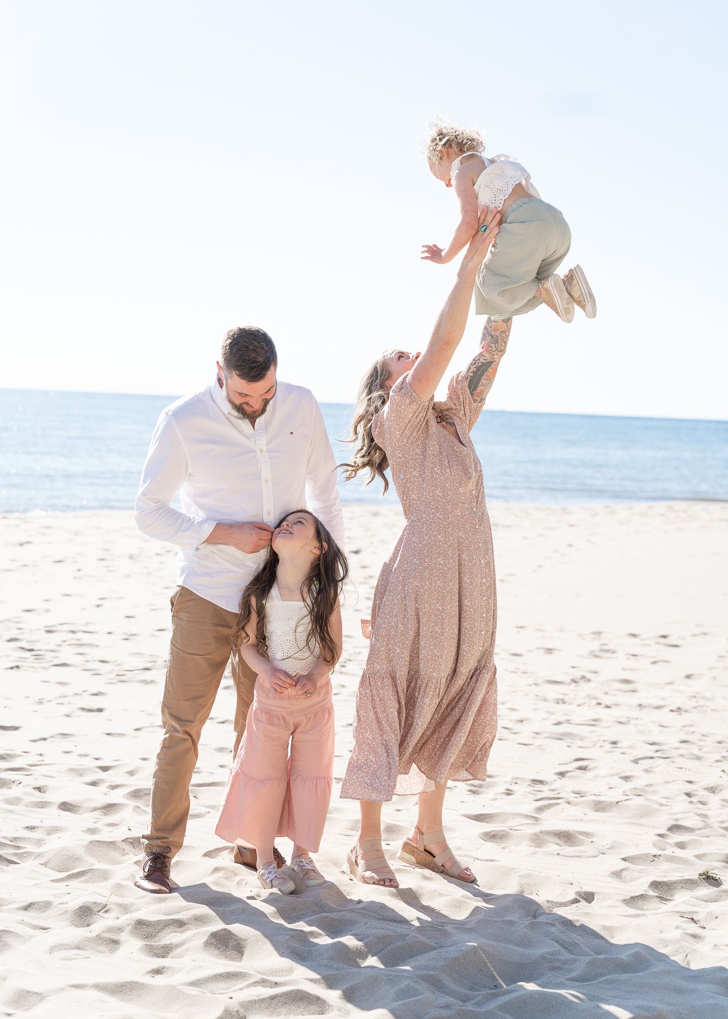 Family playing together and having fun on a sunny beach with gentle waves in the background.