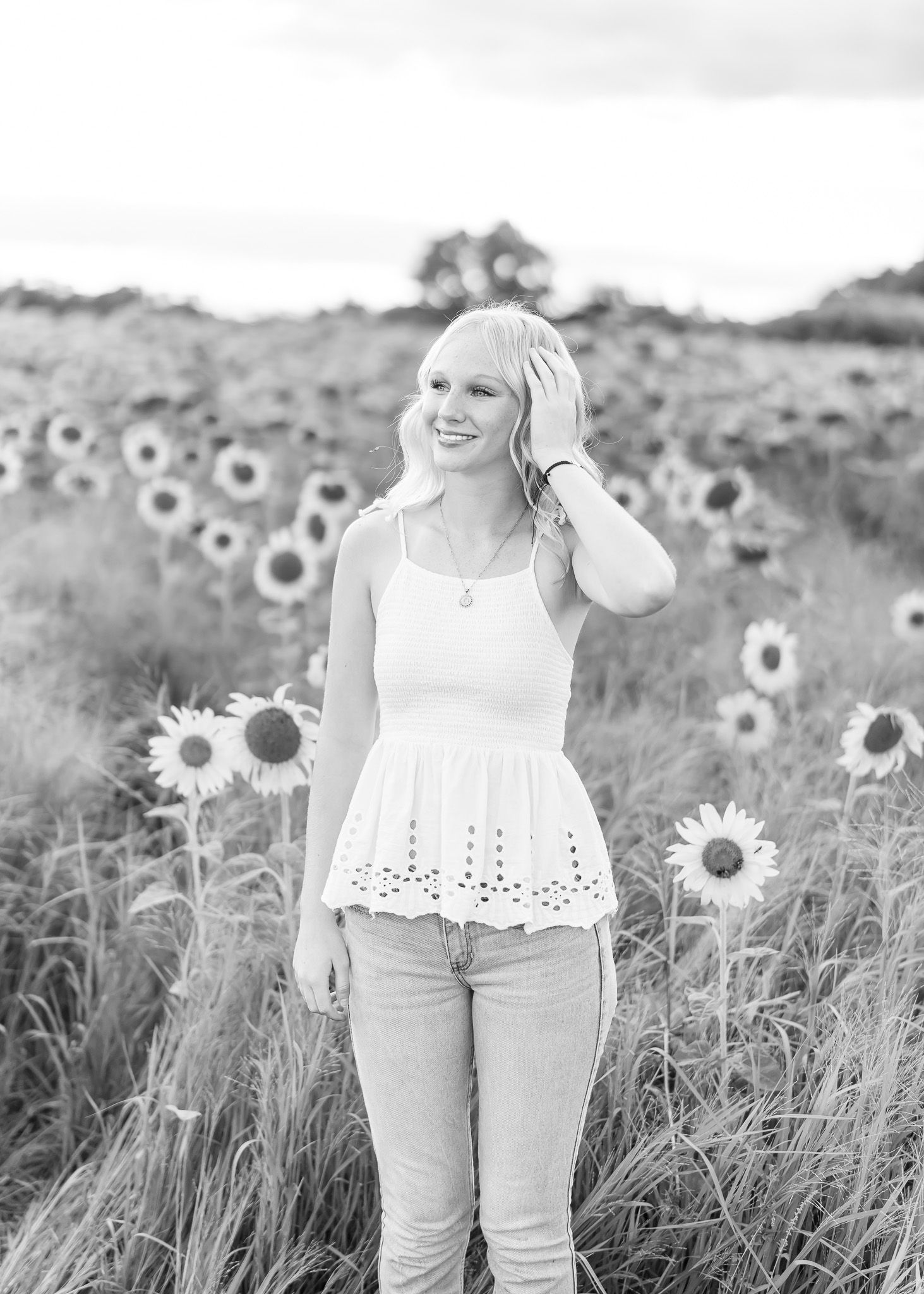 A person in a white eyelet top walks through a sunny field of blooming sunflowers on a summer day.