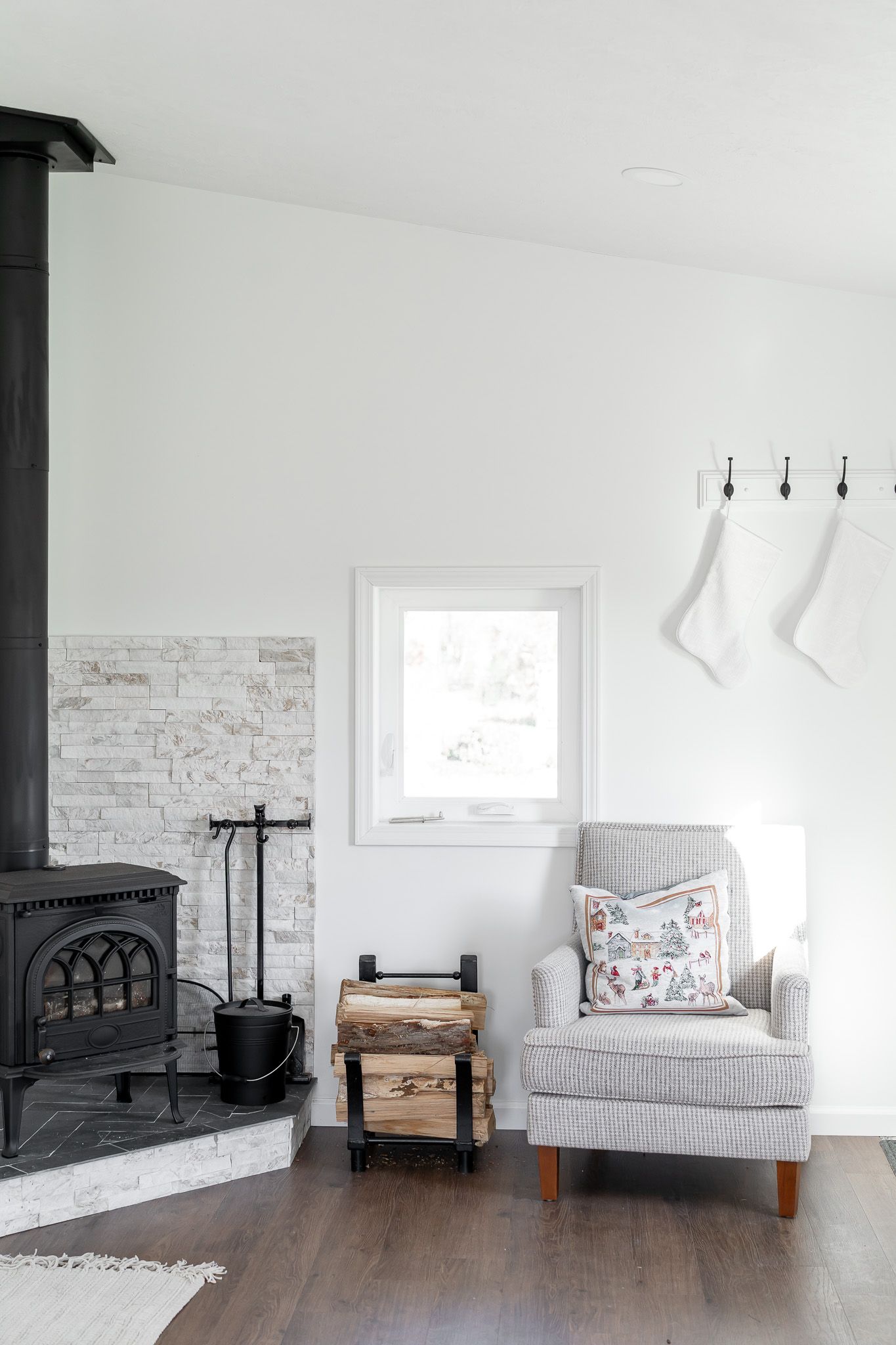 A cozy reading nook with a gray armchair and wood stove against white brick walls.