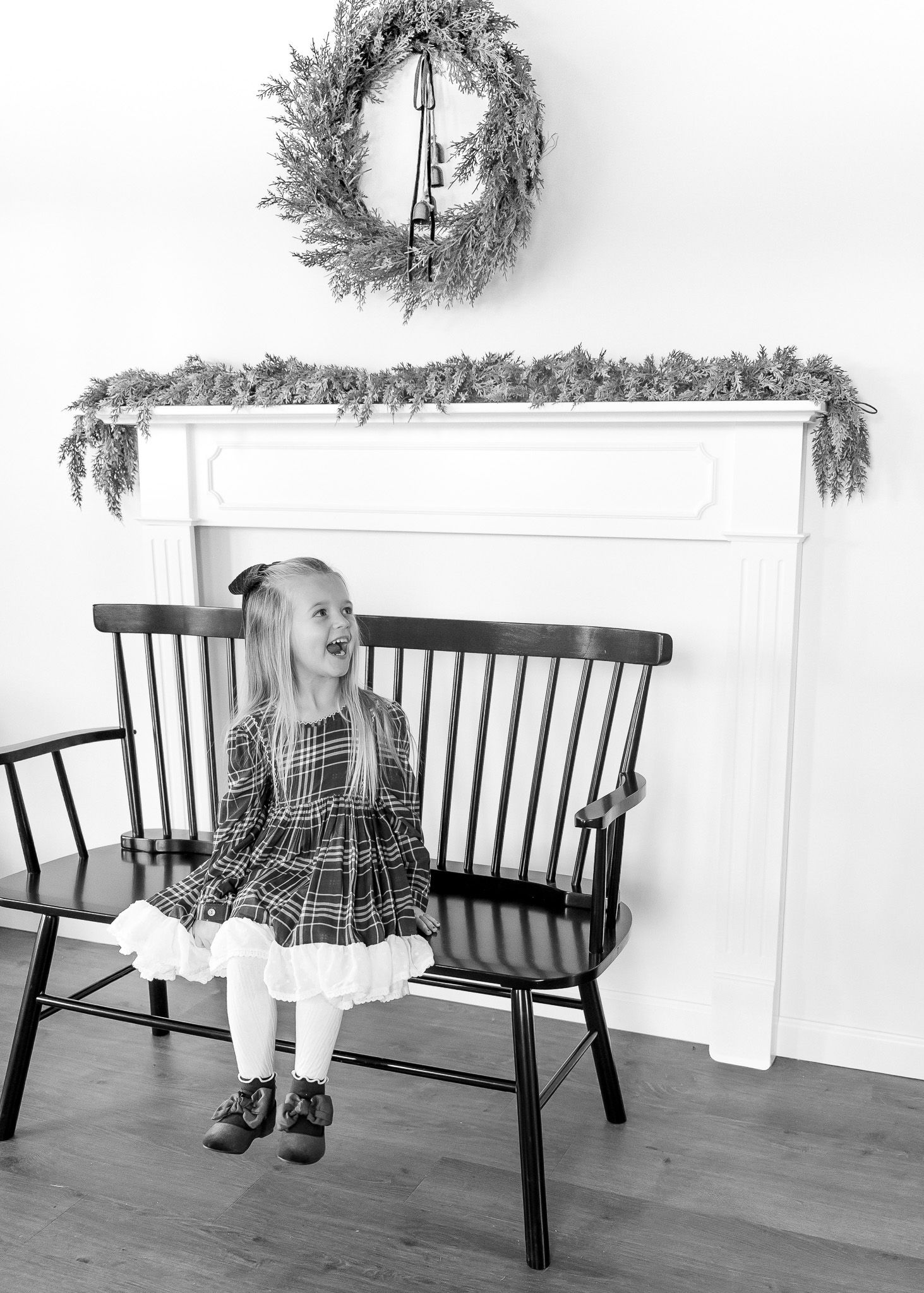 Black wooden bench with holiday wreaths and white decor against a bright wall.