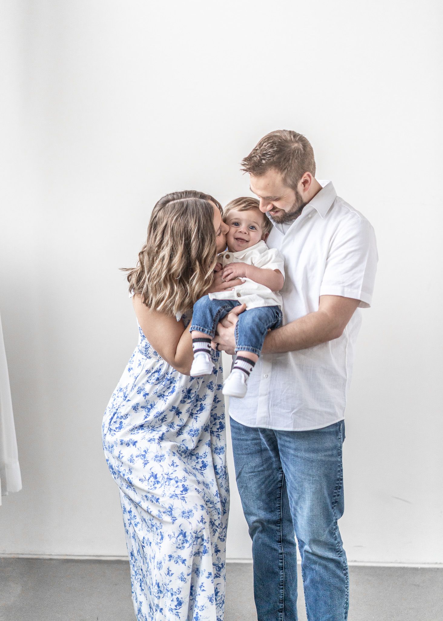 Family in matching white and blue outfits share tender moments during a lifestyle photoshoot against white backdrop.
