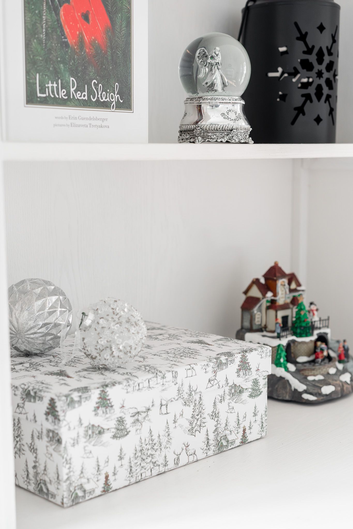 Decorative white gift boxes with winter forest patterns displayed on white shelves with holiday decor.