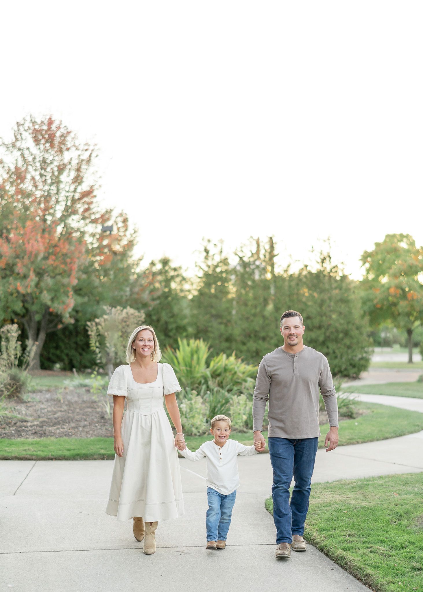 Family walking together on a paved path through a park during sunset in casual attire.