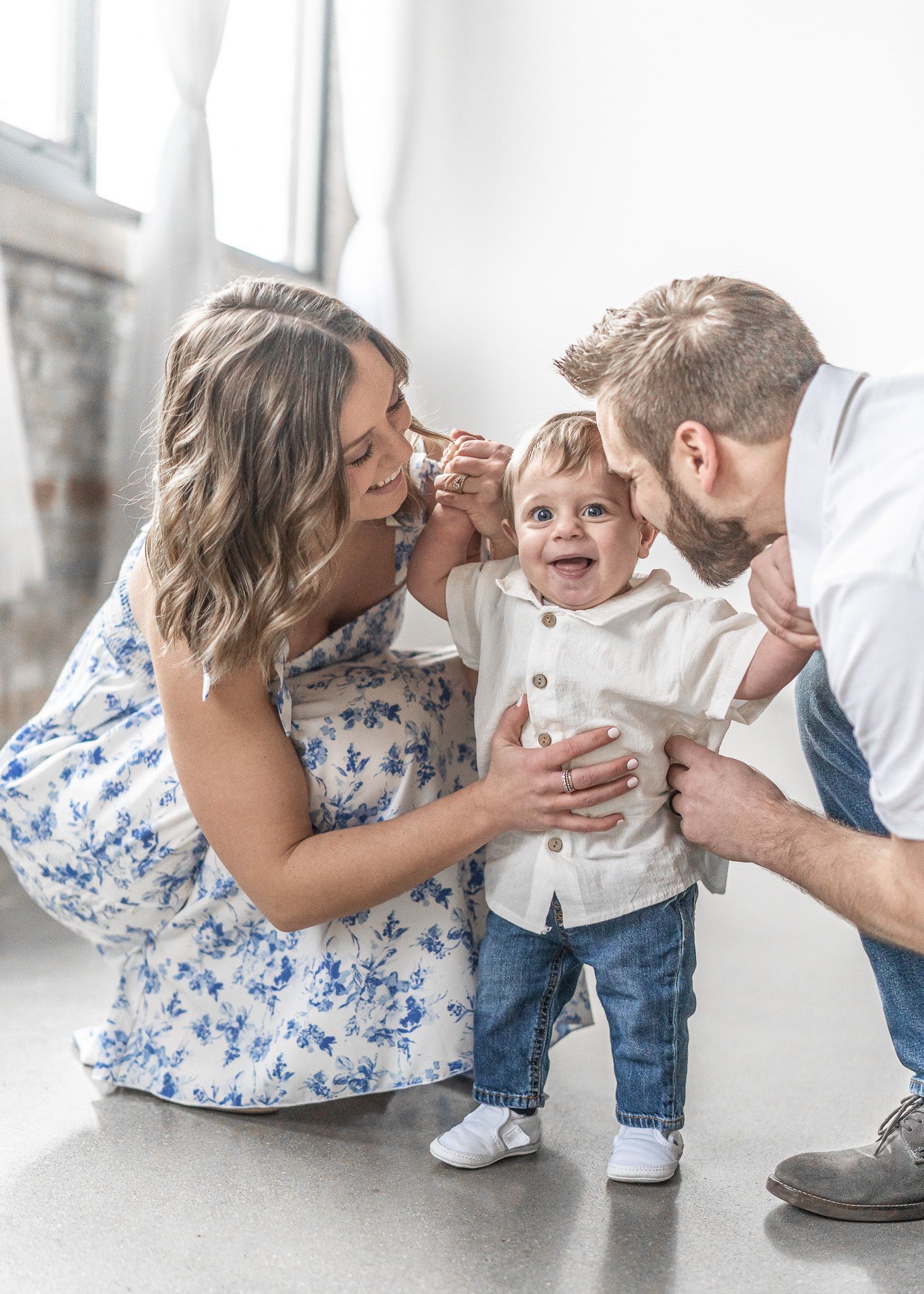 Family shares joyful moments together in a bright white studio setting with matching blue and white outfits.