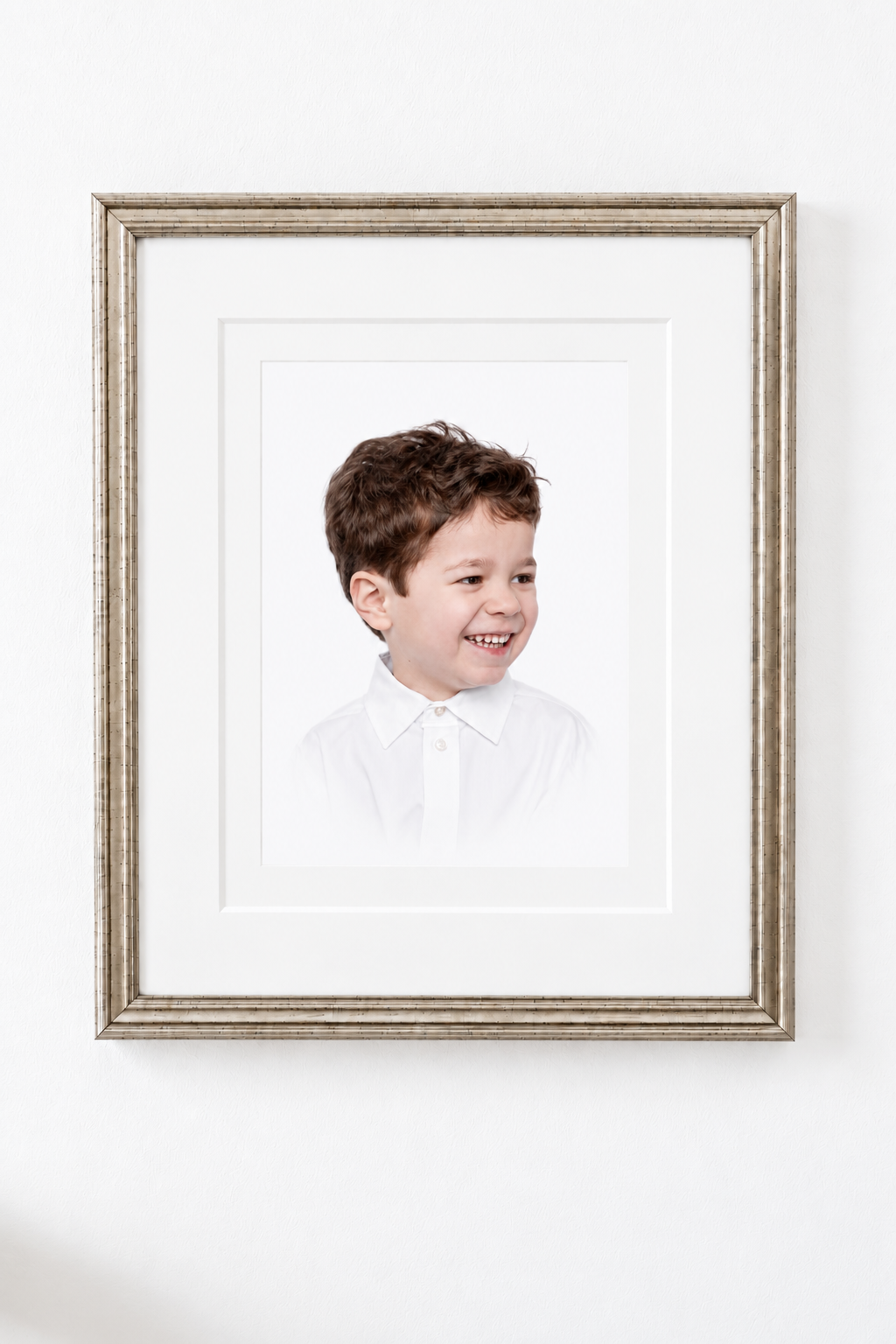 Framed portrait of a smiling young boy with brown hair wearing a white collared shirt, displayed on a white wall.