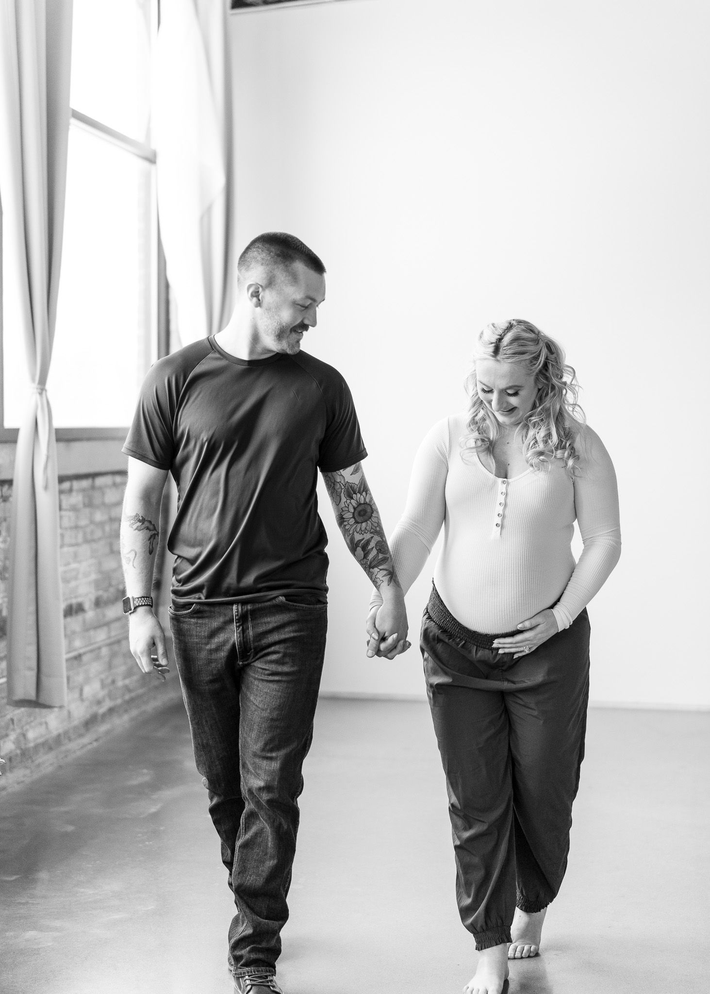 Black and white intimate photo of a couple walking together and holding hands in a bright indoor space.