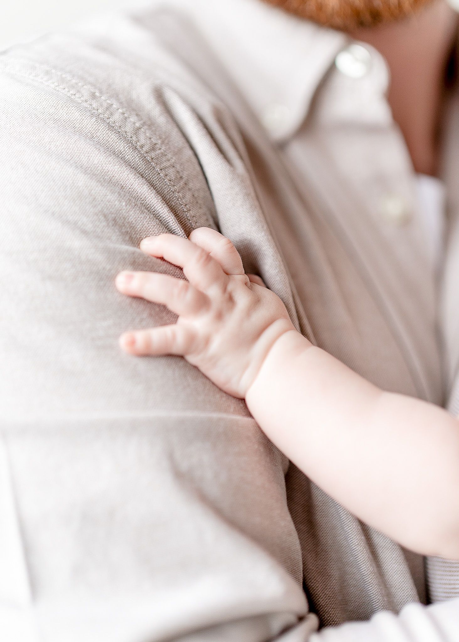 A small baby's hand grasps the soft gray fabric of someone's clothing in a tender moment.