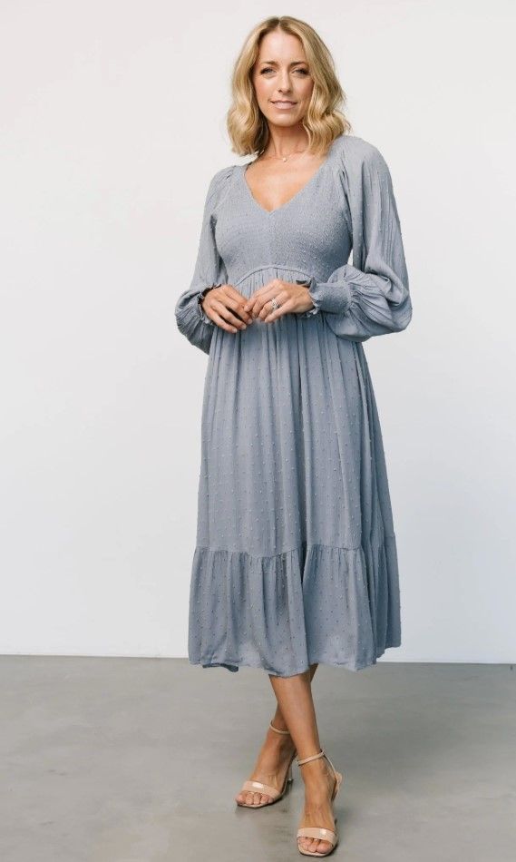 Slate blue empire waist dress with long sleeves and tiered skirt shown in studio setting.