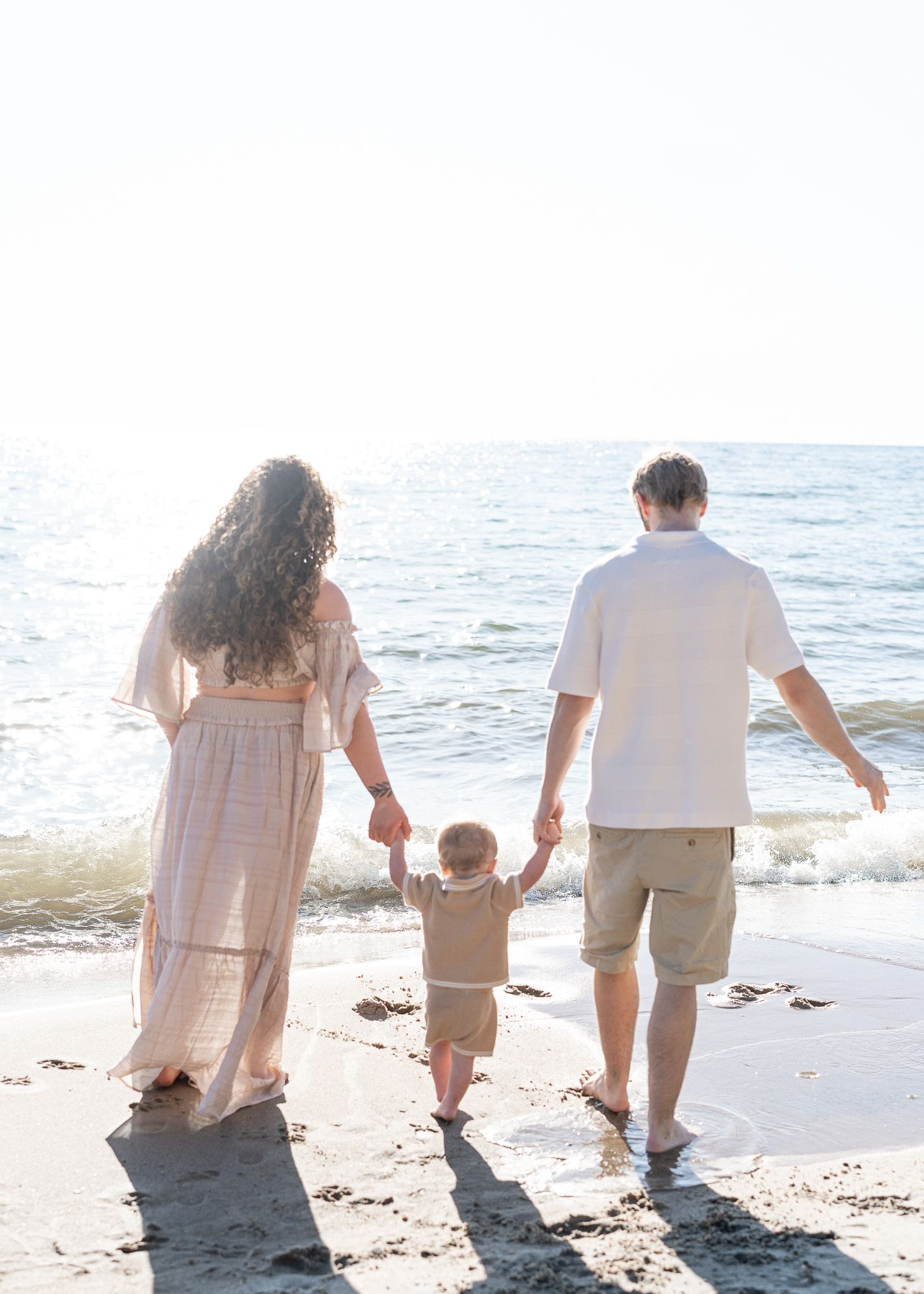 Family walking together along a scenic beach shoreline at sunset, photographed from behind.