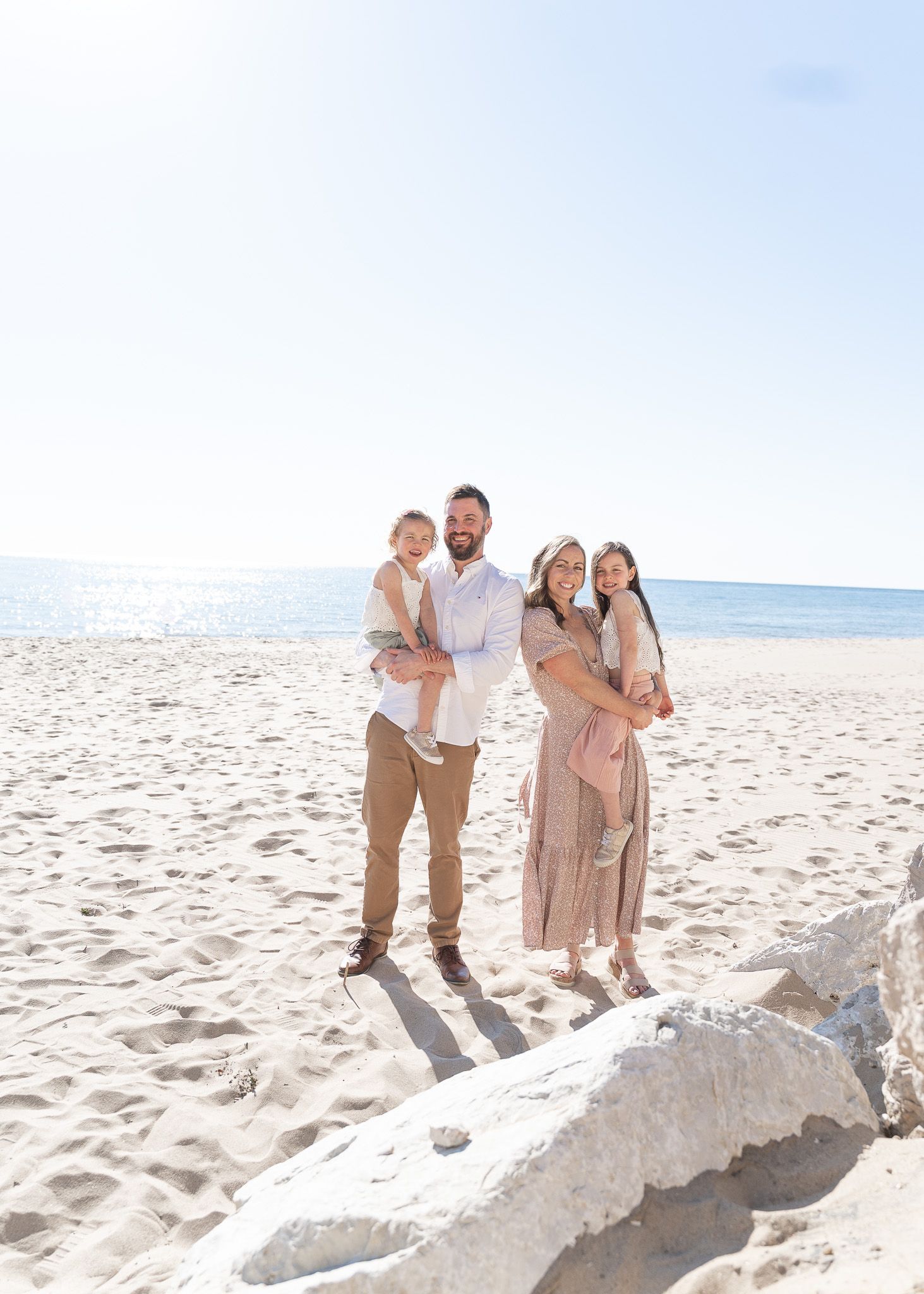A group poses together on a sandy beach, standing on a large piece of driftwood against an ocean backdrop.