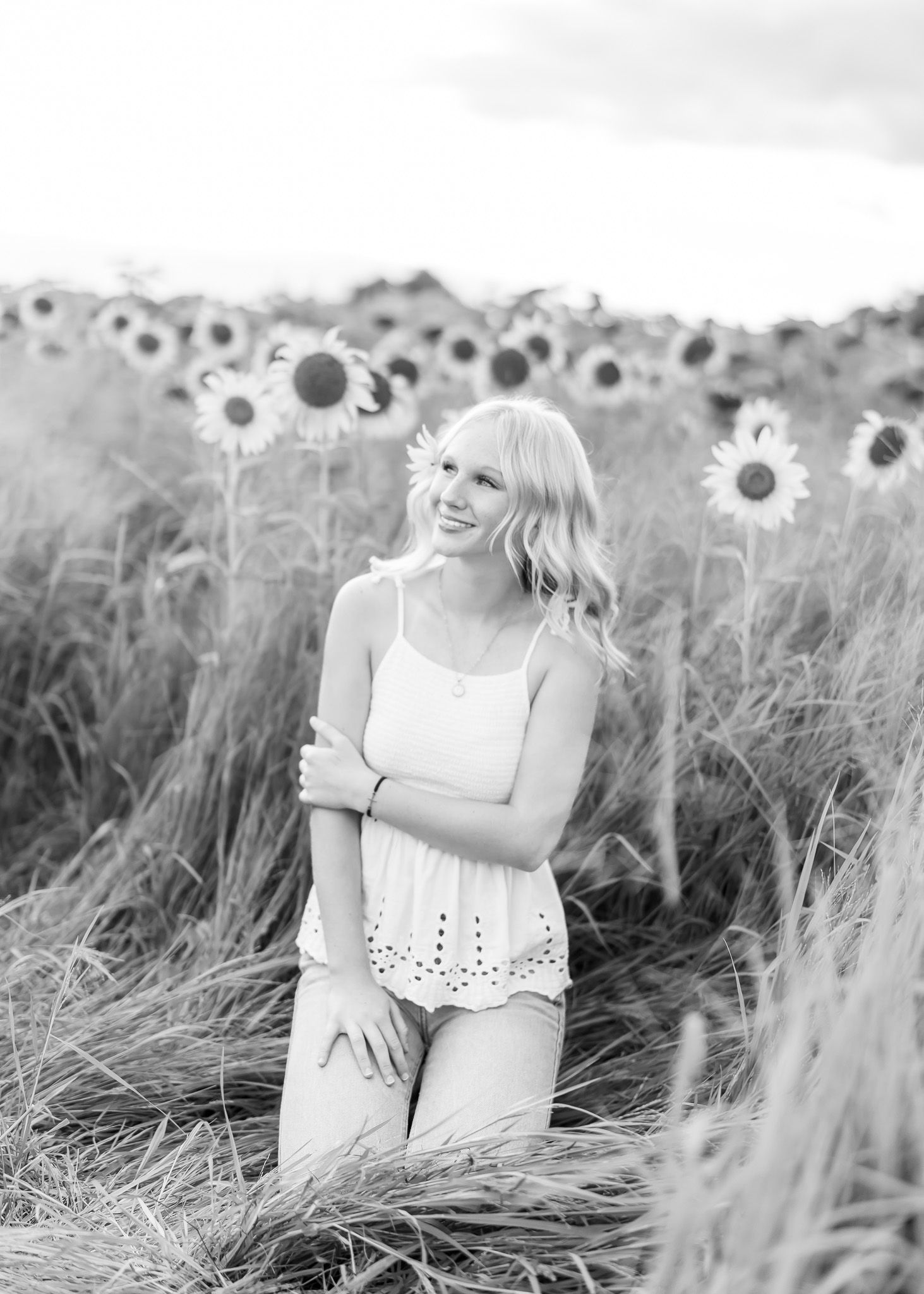 A dreamy black and white photo series showing a woman in a white dress walking through a sunflower field.