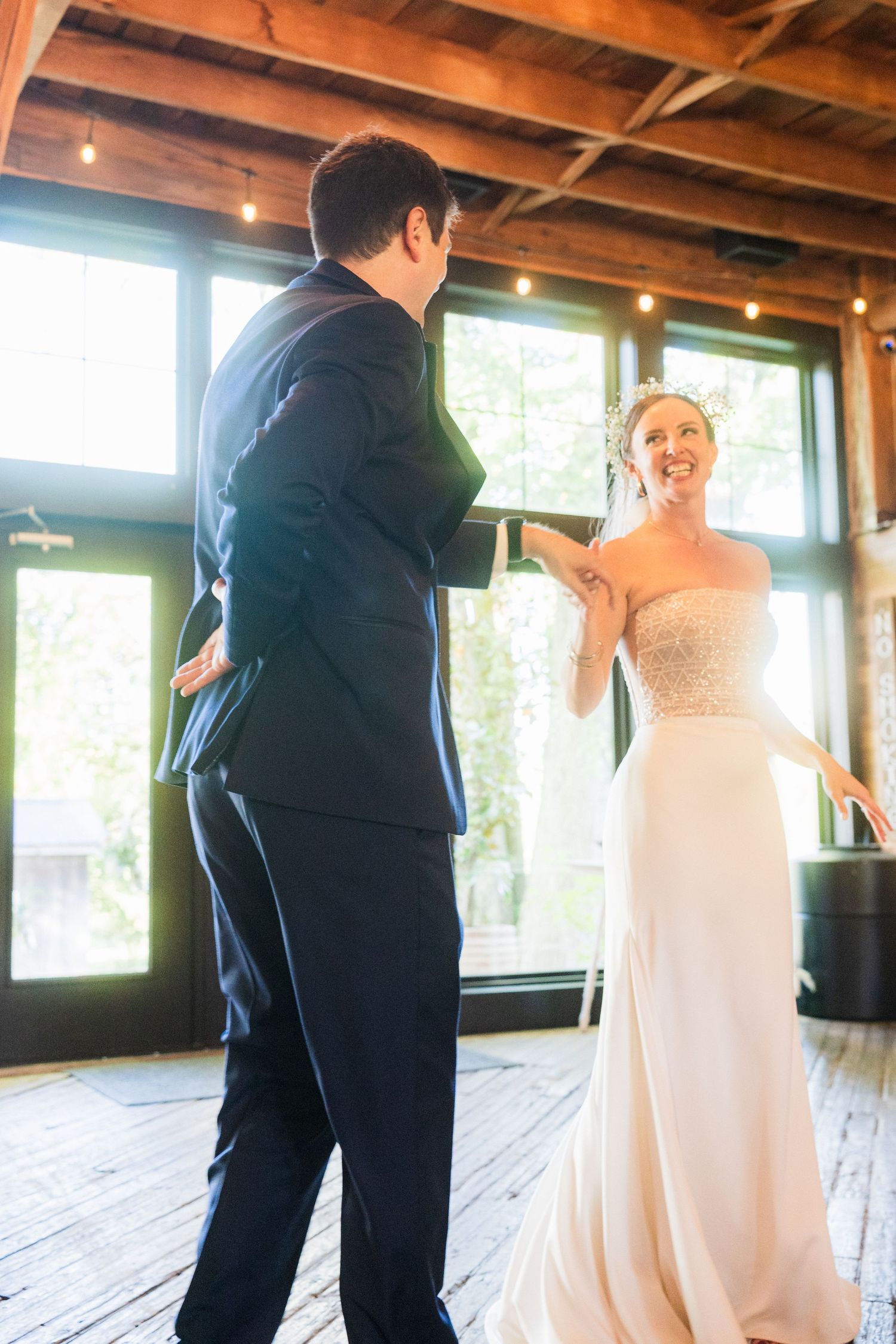 A wedding couple shares an intimate moment during their first dance in a rustic venue with wooden beams.