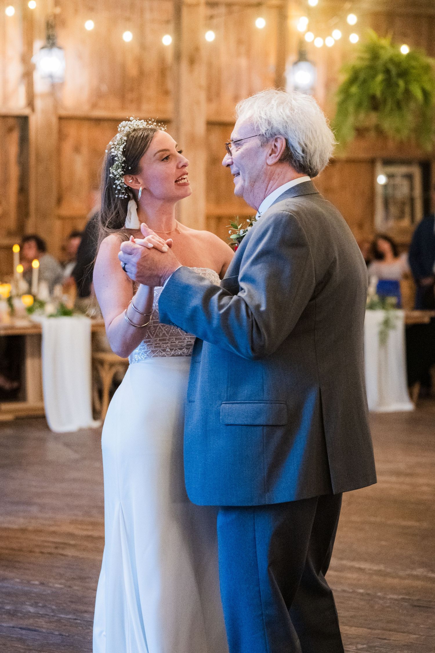 A dance moment captured in a rustic barn venue with string lights and wooden beams.