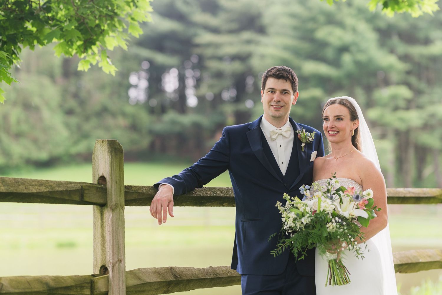 A couple poses together by a wooden fence in a lush garden setting.  at shady elms farm pittsburgh pa photography and video