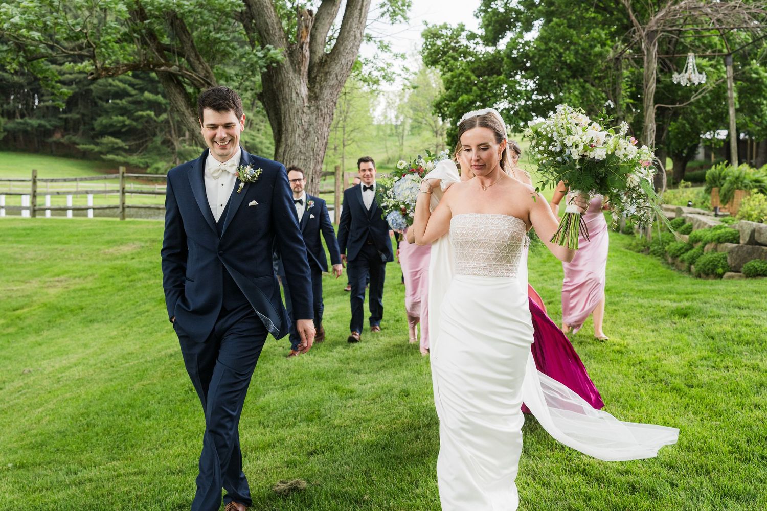 Wedding party walking across a lush green lawn with bridesmaids in colorful dresses.  at shady elms farm pittsburgh pa photography and vide