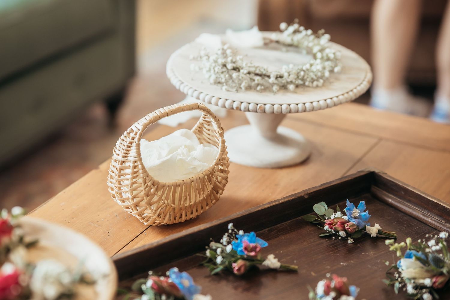 Wedding jewelry and accessories displayed on an elegant white cake stand with scattered decorative items on a wooden table.