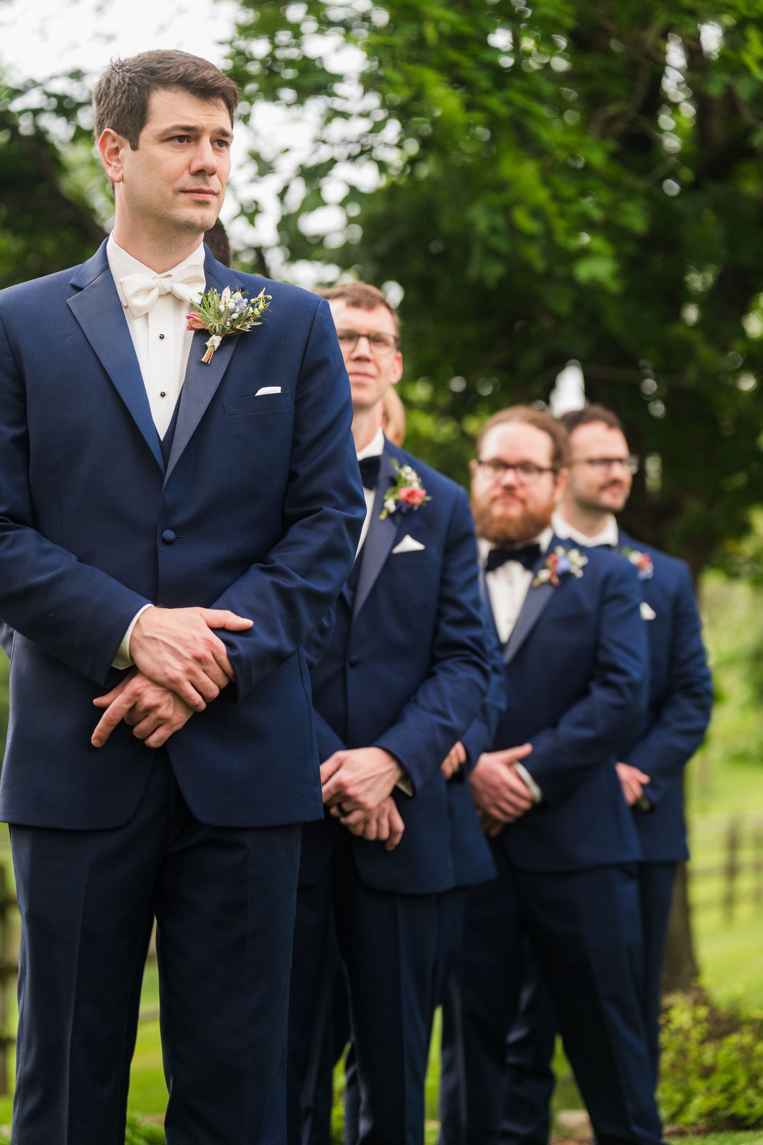 Groomsmen in navy blue suits stand in a formal lineup during an outdoor wedding ceremony.  at shady elms farm pittsburgh pa photography and
