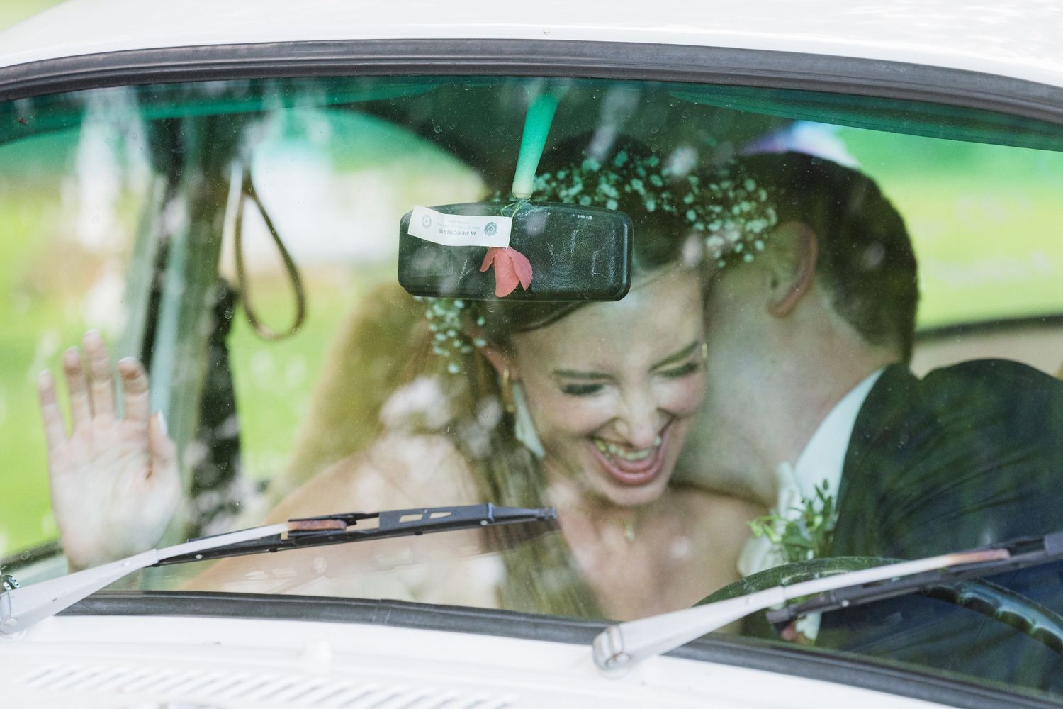 A joyful couple shares a romantic moment inside a vintage car on their wedding day, captured through the windshield.