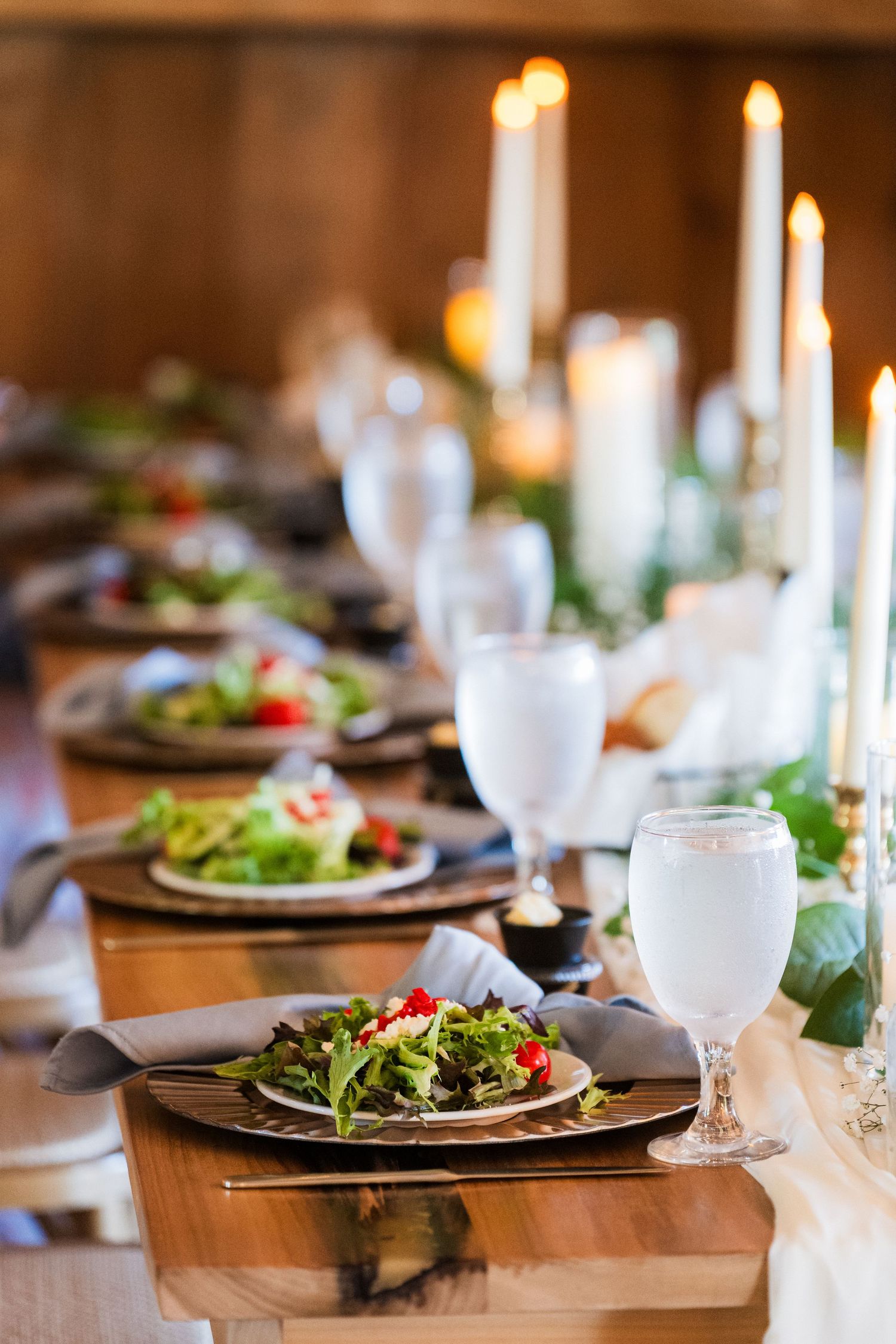 Elegant wedding reception table settings with salads and glowing candles in a rustic venue.