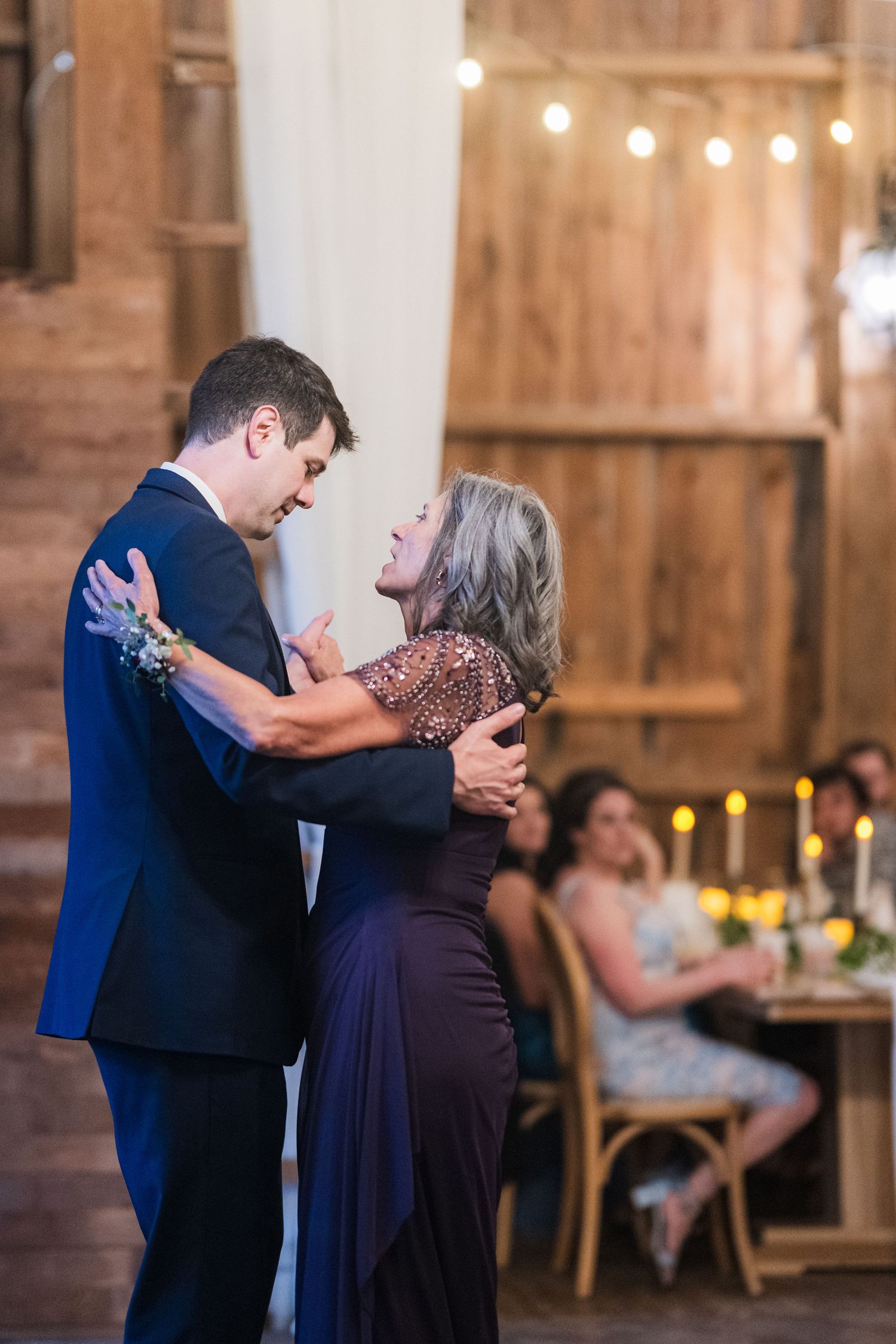 Wedding reception dance between guests in a rustic barn venue with string lights.