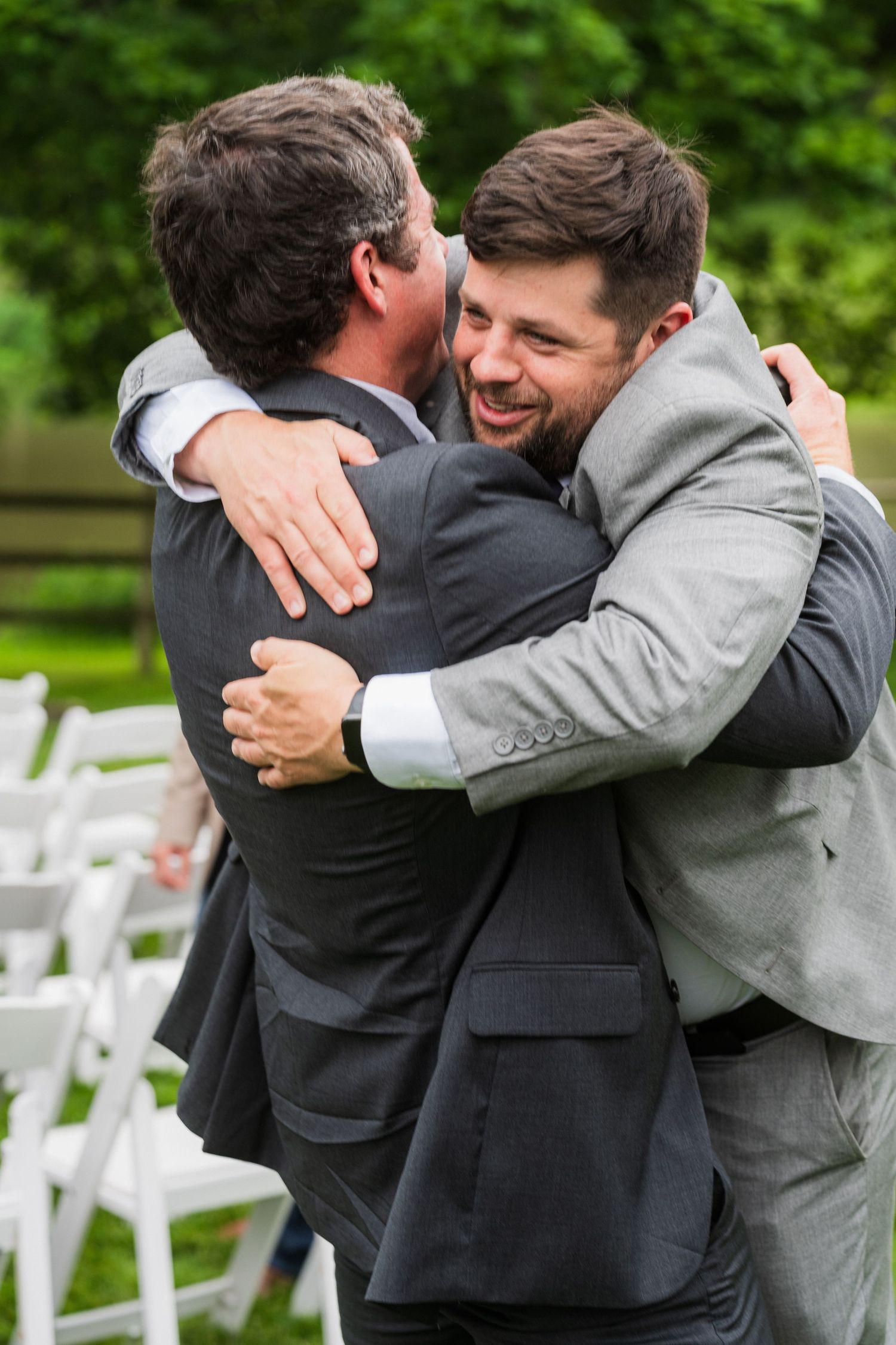 at shady elms fSequential photos show two men in formal attire sharing an emotional embrace at an outdoor wedding venue with white chairs.