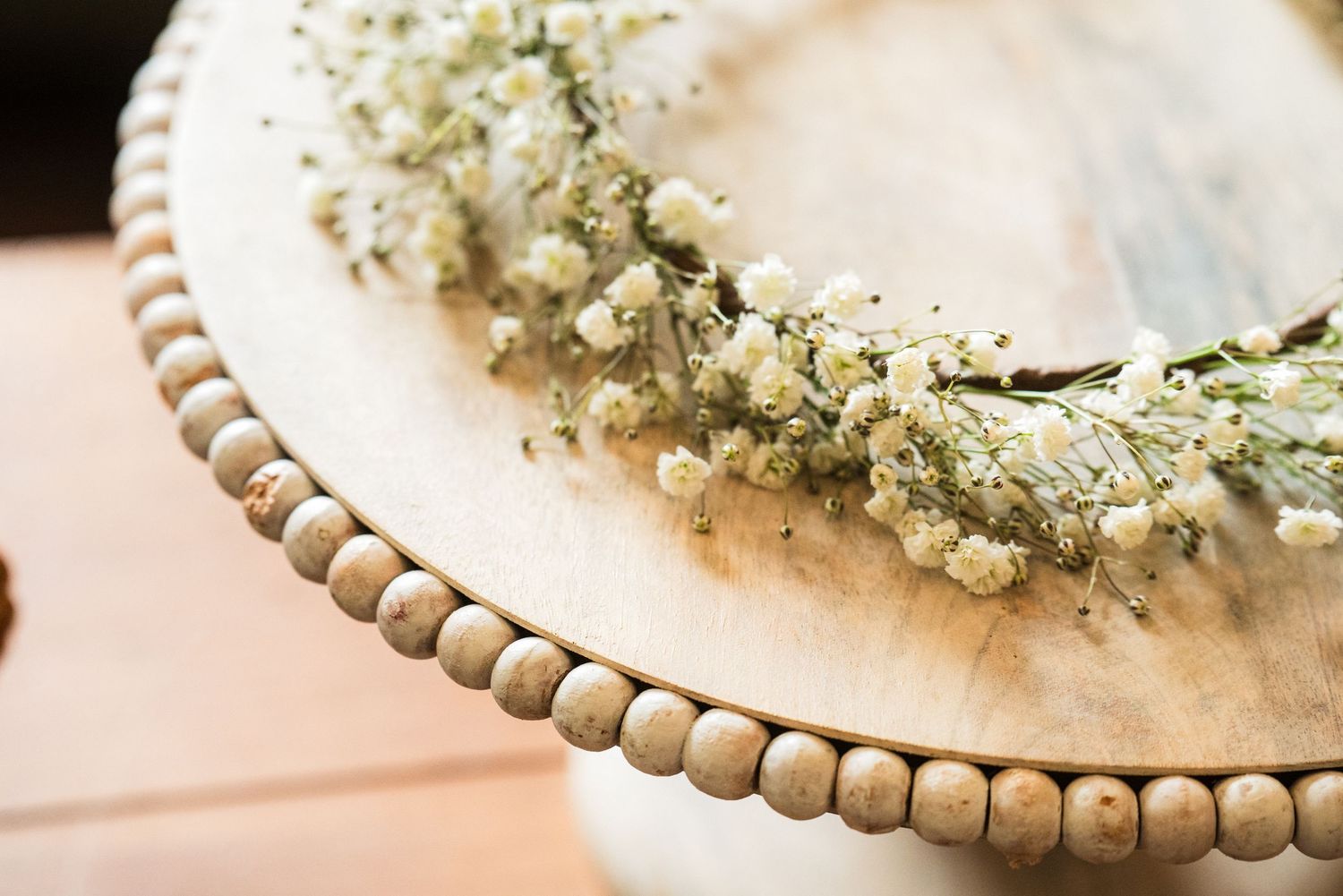 A delicate baby's breath flower crown rests on a wooden beaded plate edge.