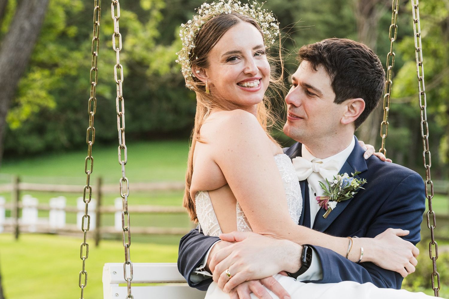 A joyful wedding couple embraces while sitting together on an outdoor swing.