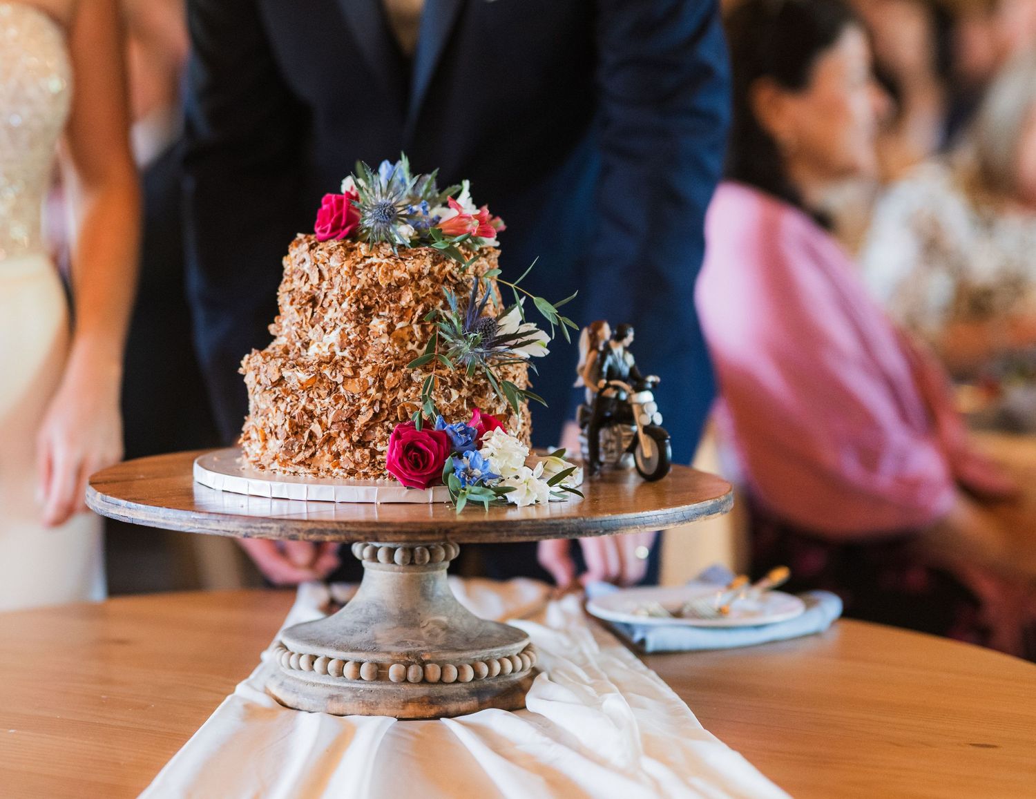 Rustic chocolate cake decorated with succulents and bright flowers on an ornate silver cake stand.