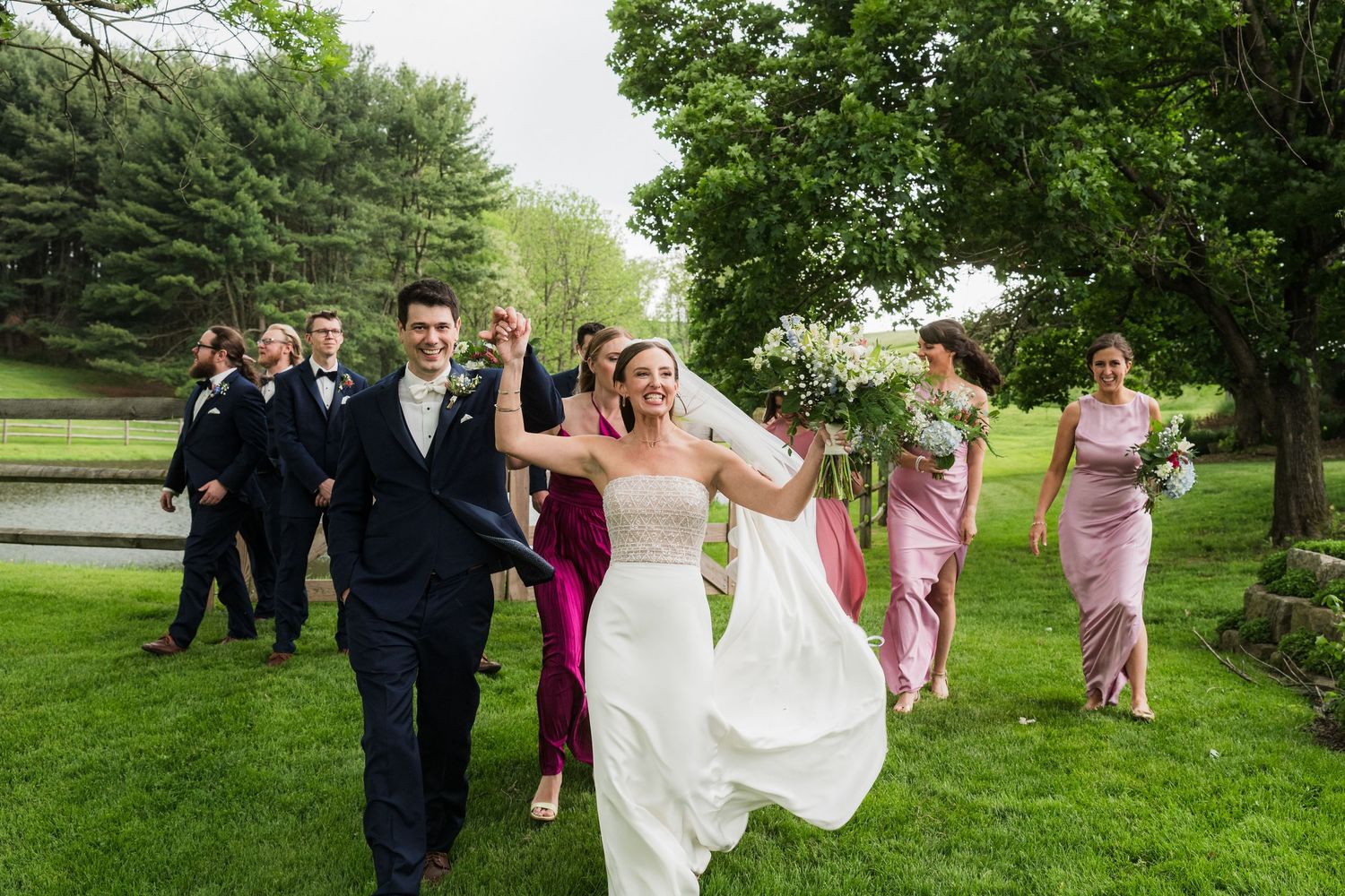 Wedding party walking and laughing together on a lush green lawn during spring celebration.  at shady elms farm pittsburgh pa photography a