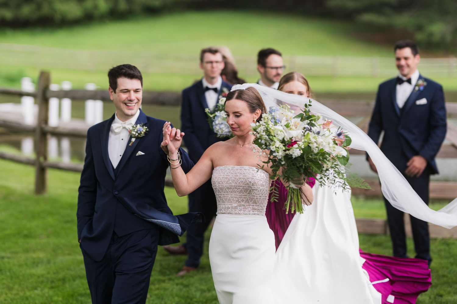 A joyful wedding couple celebrates on a grassy lawn with bridal party members visible in background.  at shady elms farm pittsburgh pa phot