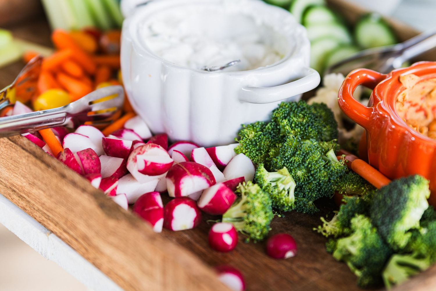 Fresh colorful vegetables including radishes, broccoli, and carrots arranged on a wooden cutting board.