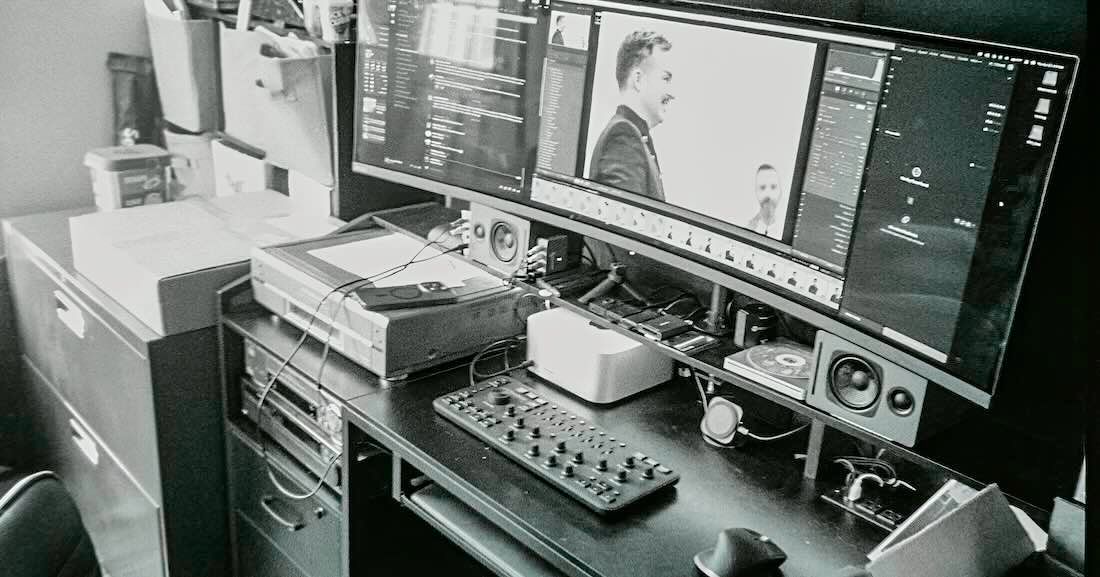 A black and white photograph of a digital workstation with dual monitors, keyboard console and production equipment.