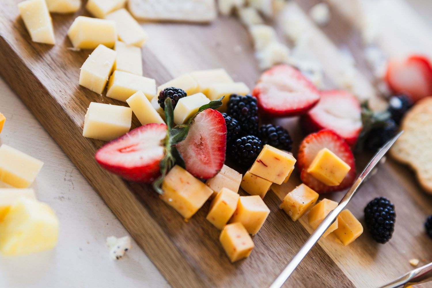Wooden charcuterie board with cubed cheese, fresh strawberries, blackberries and assorted snacks.