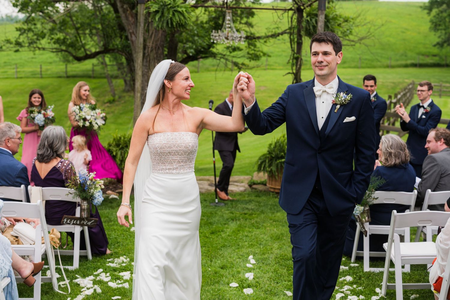 Wedding ceremony setup with white chairs on green lawn surrounded by trees.