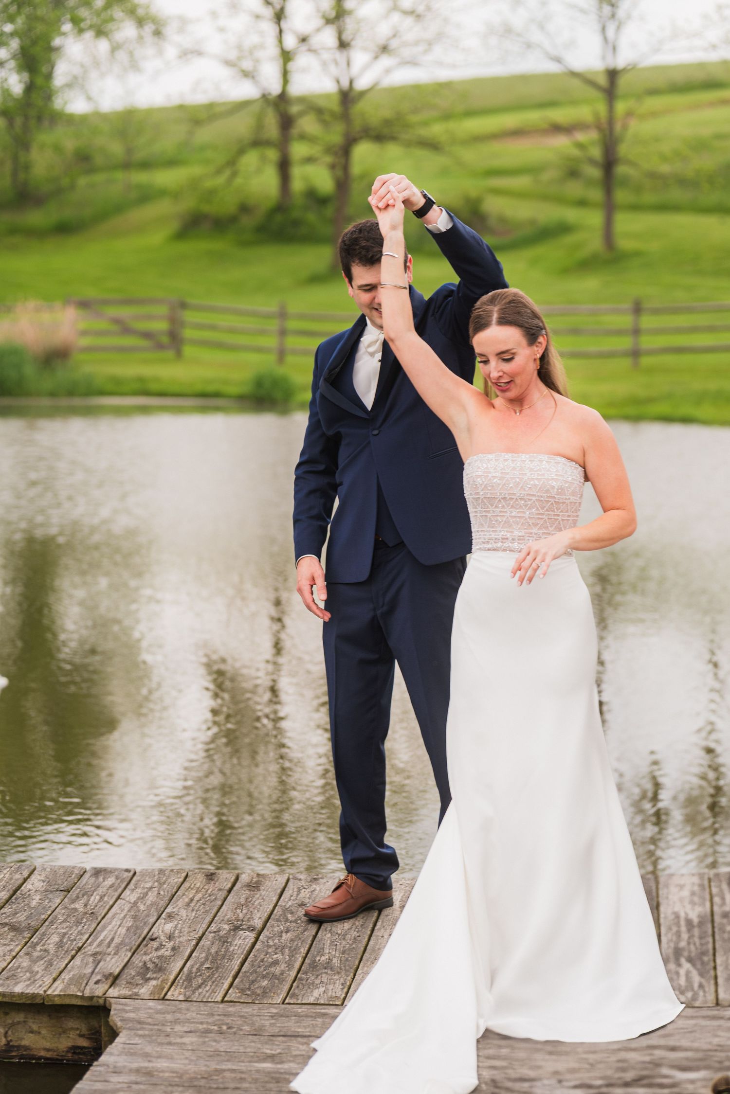 Wedding couple dancing together on wooden dock overlooking scenic lake and hills.