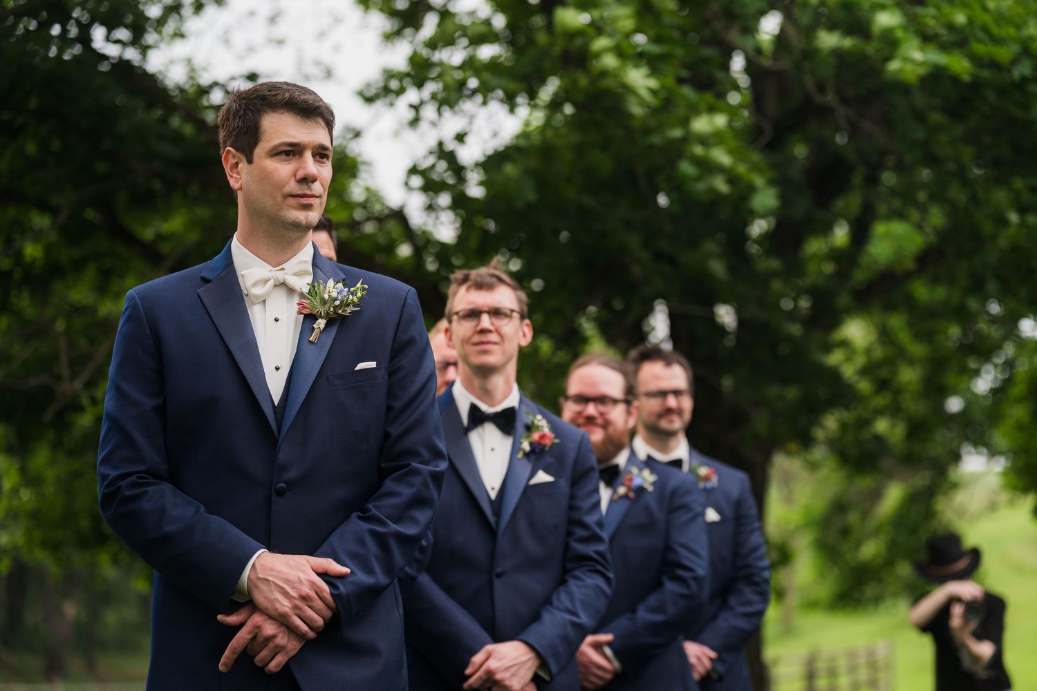 Groomsmen in navy suits stand in line during an outdoor wedding ceremony.  at shady elms farm pittsburgh pa photography and video