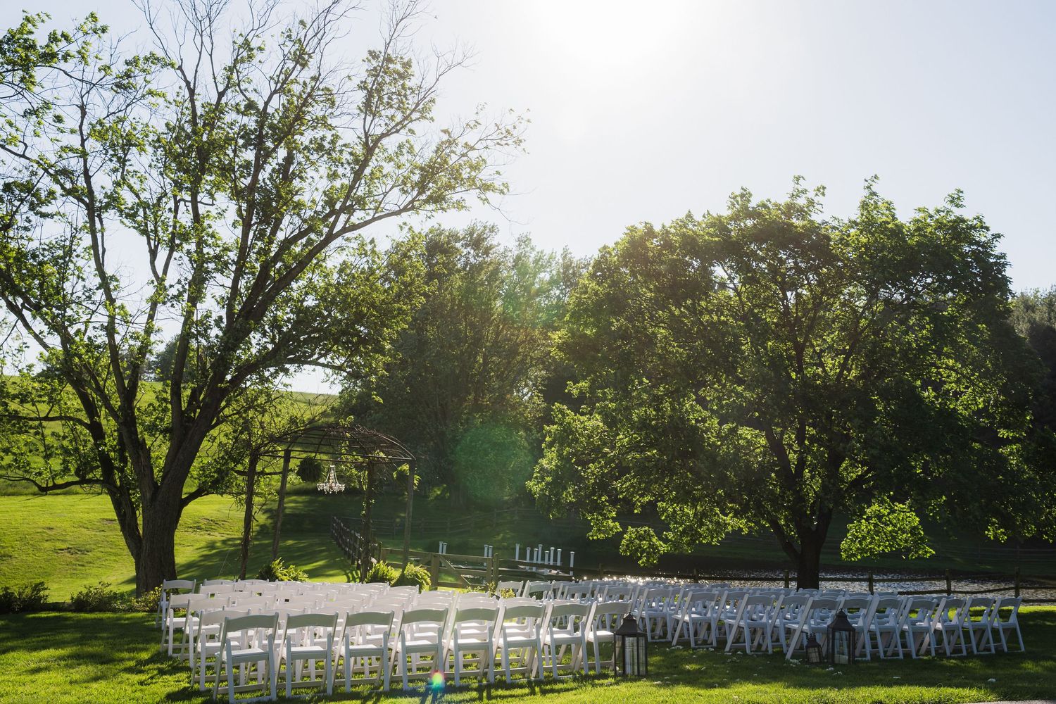 White chairs set up for an outdoor wedding ceremony under mature trees on a sunny day.  at shady elms farm pittsburgh pa photography and vi