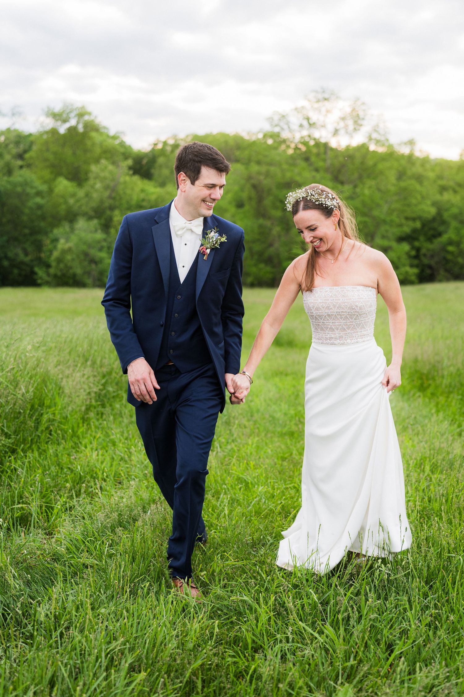 Candid wedding photo of couple walking through sun-lit meadow.
