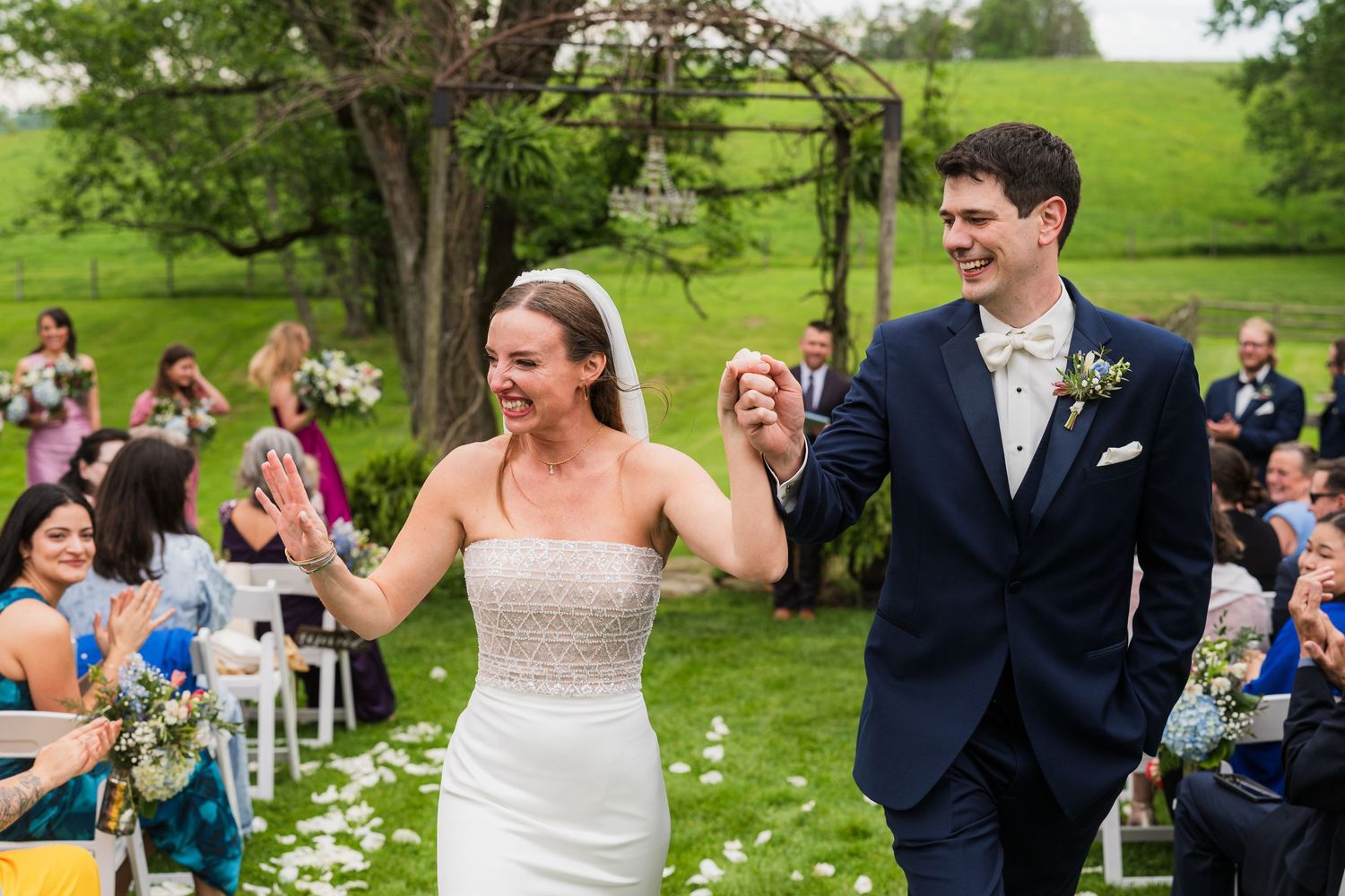 Wedding party celebrating outdoors on a beautiful spring day with scattered white petals on the grass.  at shady elms farm pittsburgh pa ph