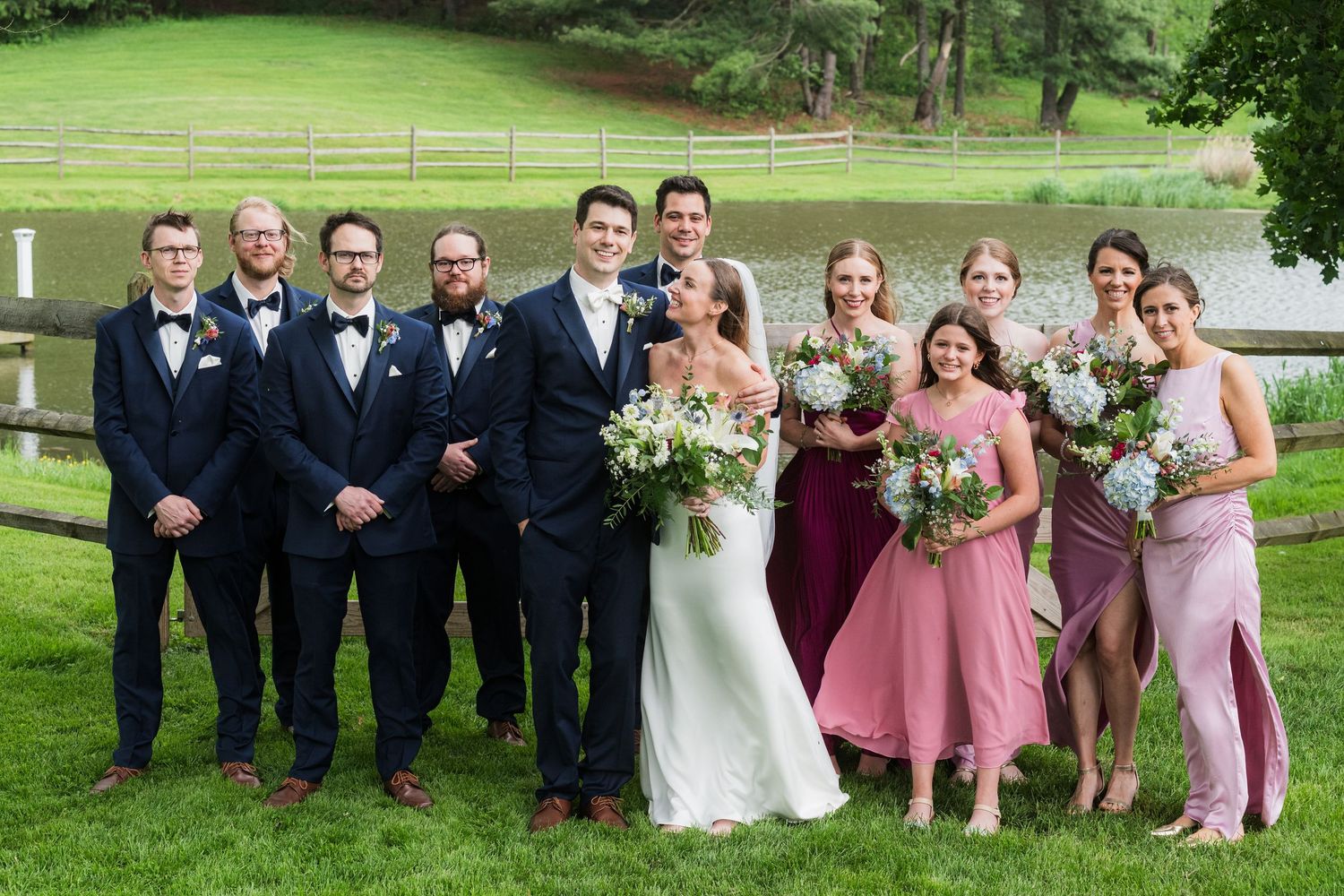 A wedding party poses outdoors on green lawn wearing navy suits and burgundy dresses.  at shady elms farm pittsburgh pa photography and vid