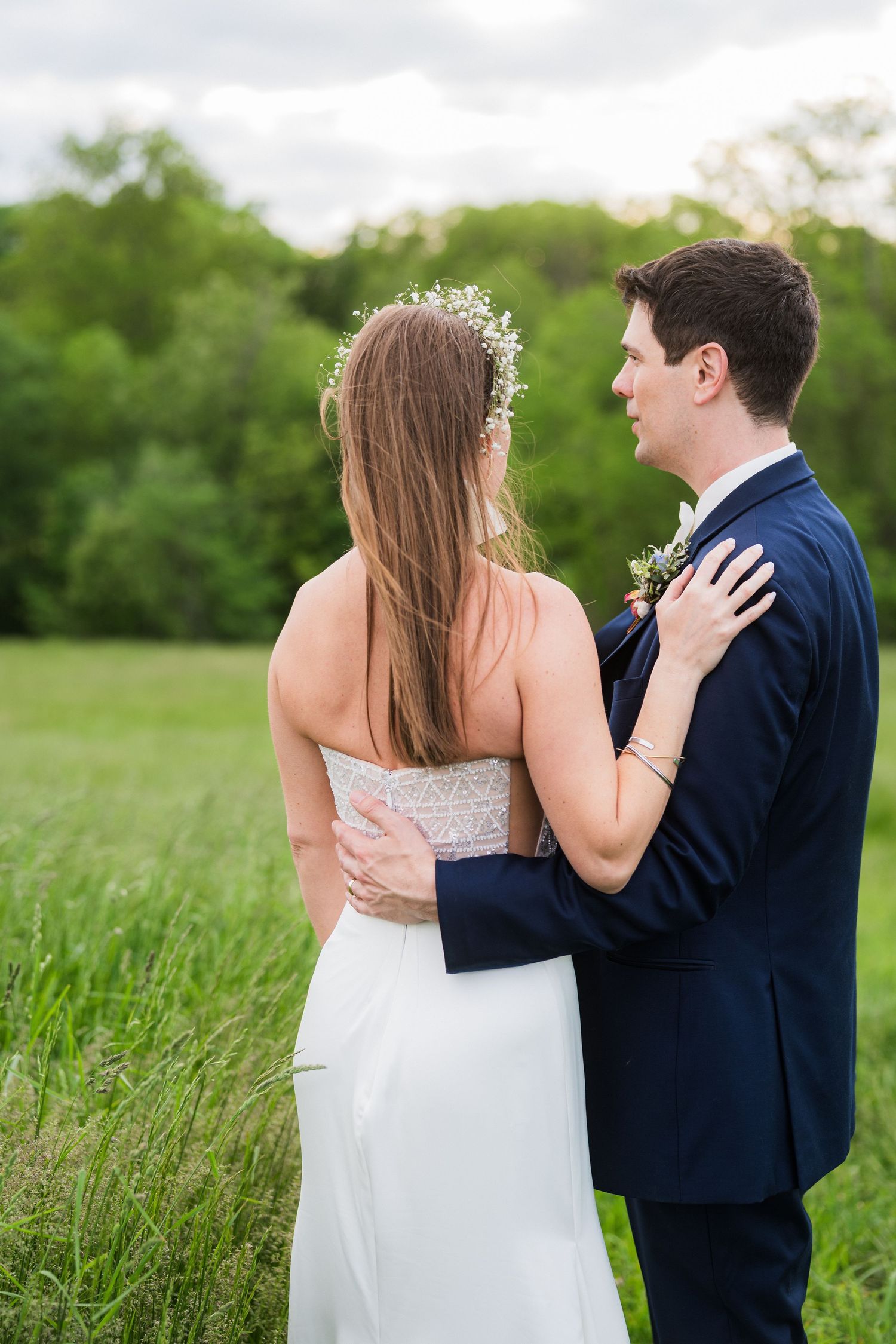 Progressive wedding photos capture tender first look moments between couple in white dress and navy suit in grassy field.