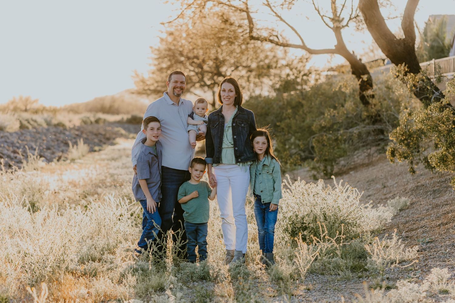 A family walks together on a desert trail during golden hour as the sun sets behind them in the Arizona landscape.
