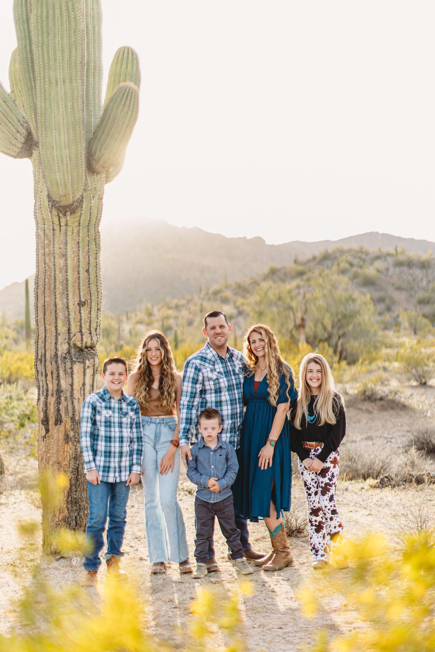 A group poses together in front of a tall saguaro cactus in the Arizona desert during golden hour.